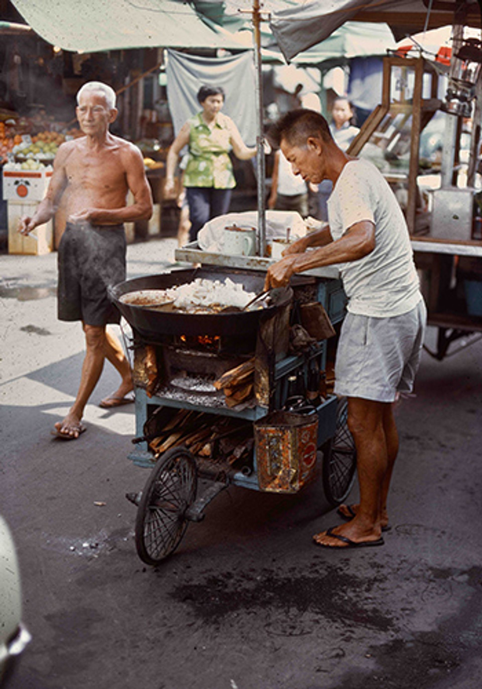 A chye tow kueh (radish cake) seller, cooking over a wood stove fire. Photographed in October 1972 at Chinatown.