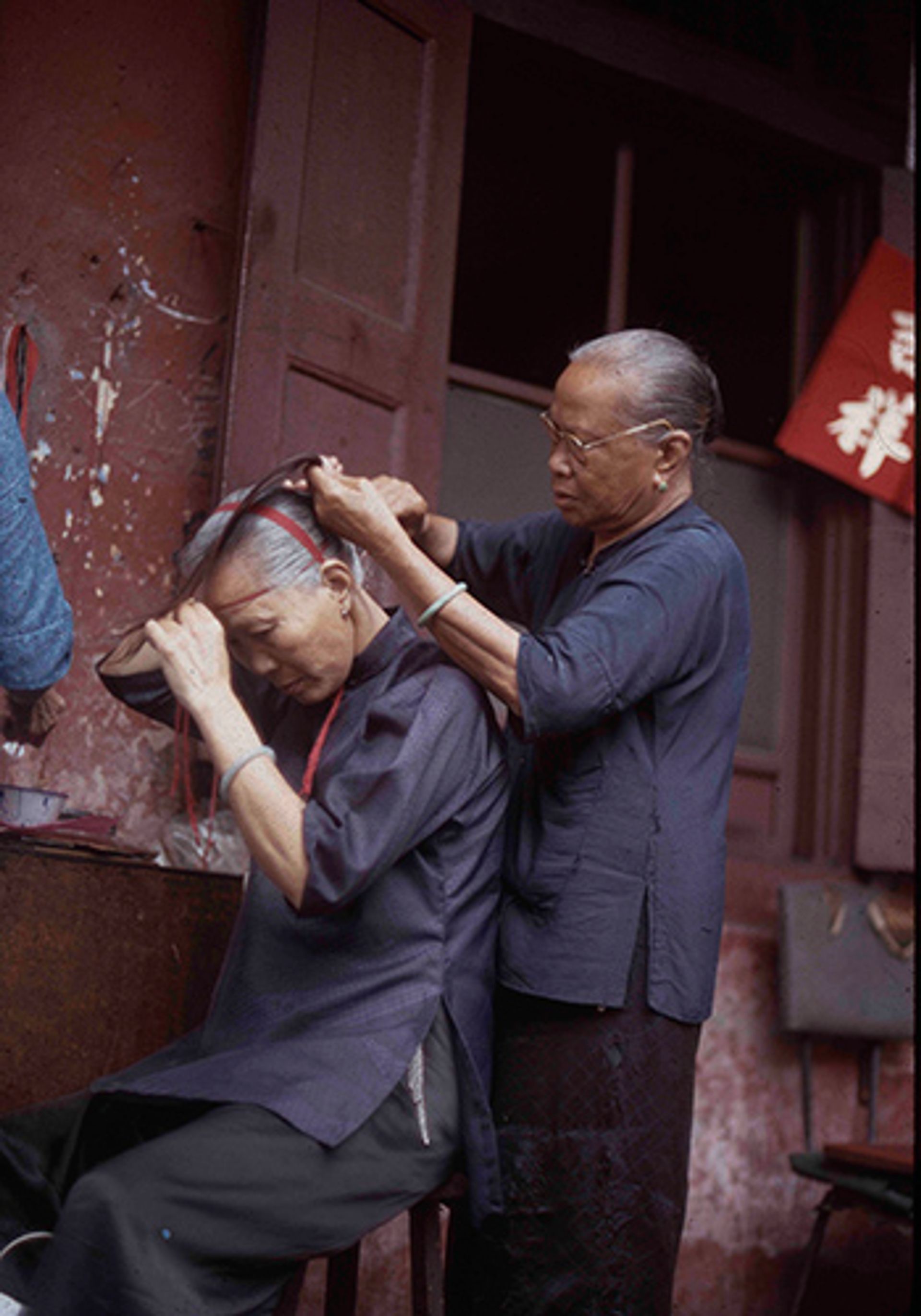 Two elderly women grooming their hair in the five-foot way along their living quarters in Chinatown. Photographed in February 1972.
