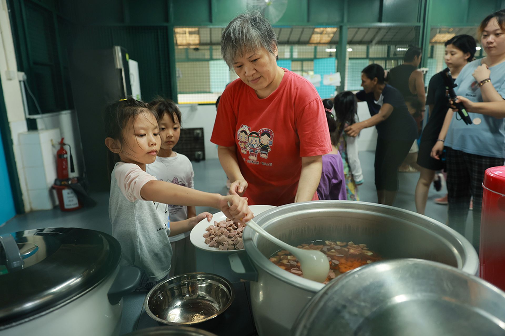 Volunteer Tan Beng Tian, 57, assists Oriana Liu (left) and Zou Jiangxin (centre) as they prepare bee hoon soup for everyone.