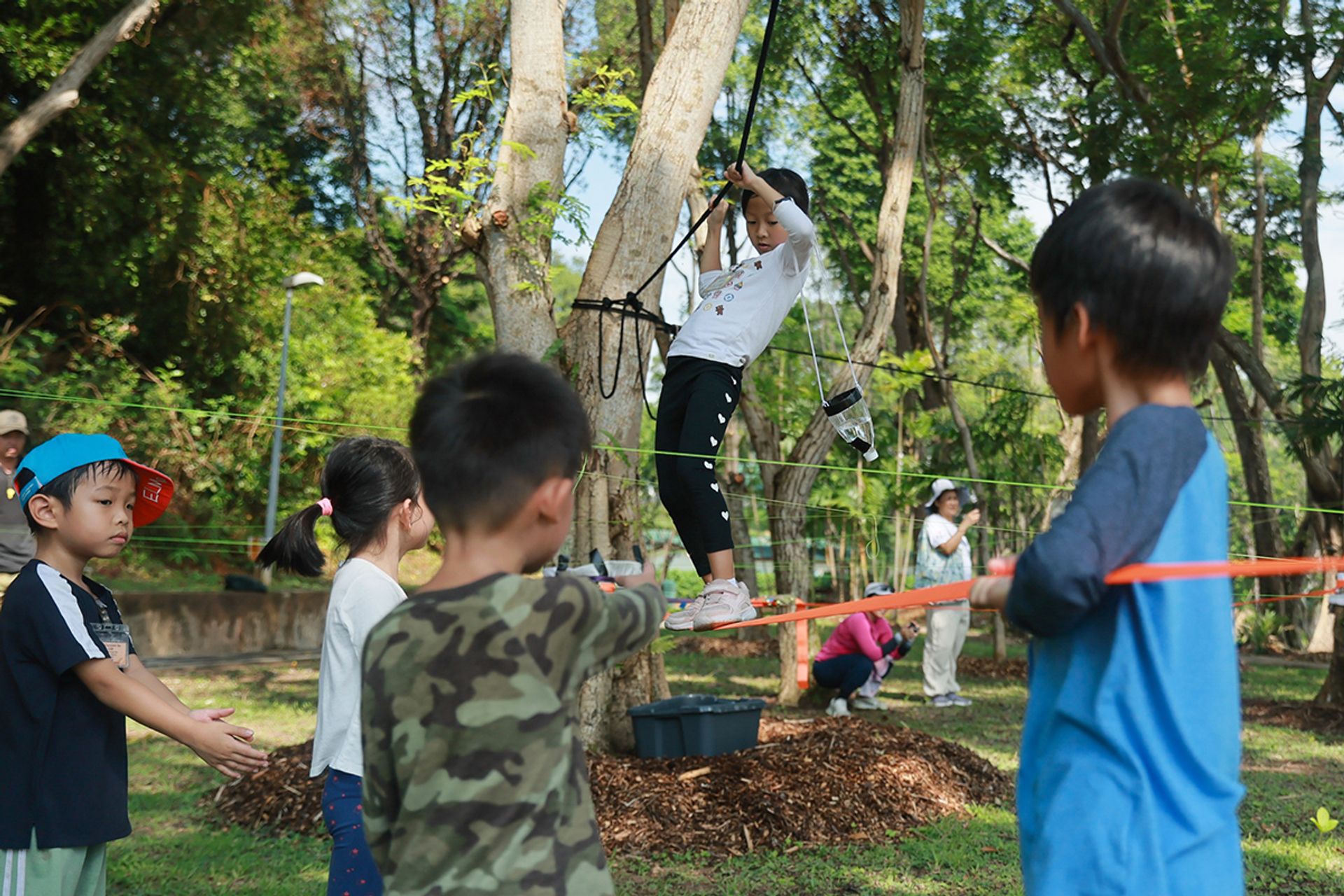 Athena Loh (second from left), Ng Zhi Qian (in green) and Wang Yan (far right) help to stabilise and support their teammate Khor Xin Yu as Hong Jingpeng (far left) watches by the side. Xin Yu is attempting the Spider Web Challenge to fetch water while walking on ropes hanging about a metre off the ground.