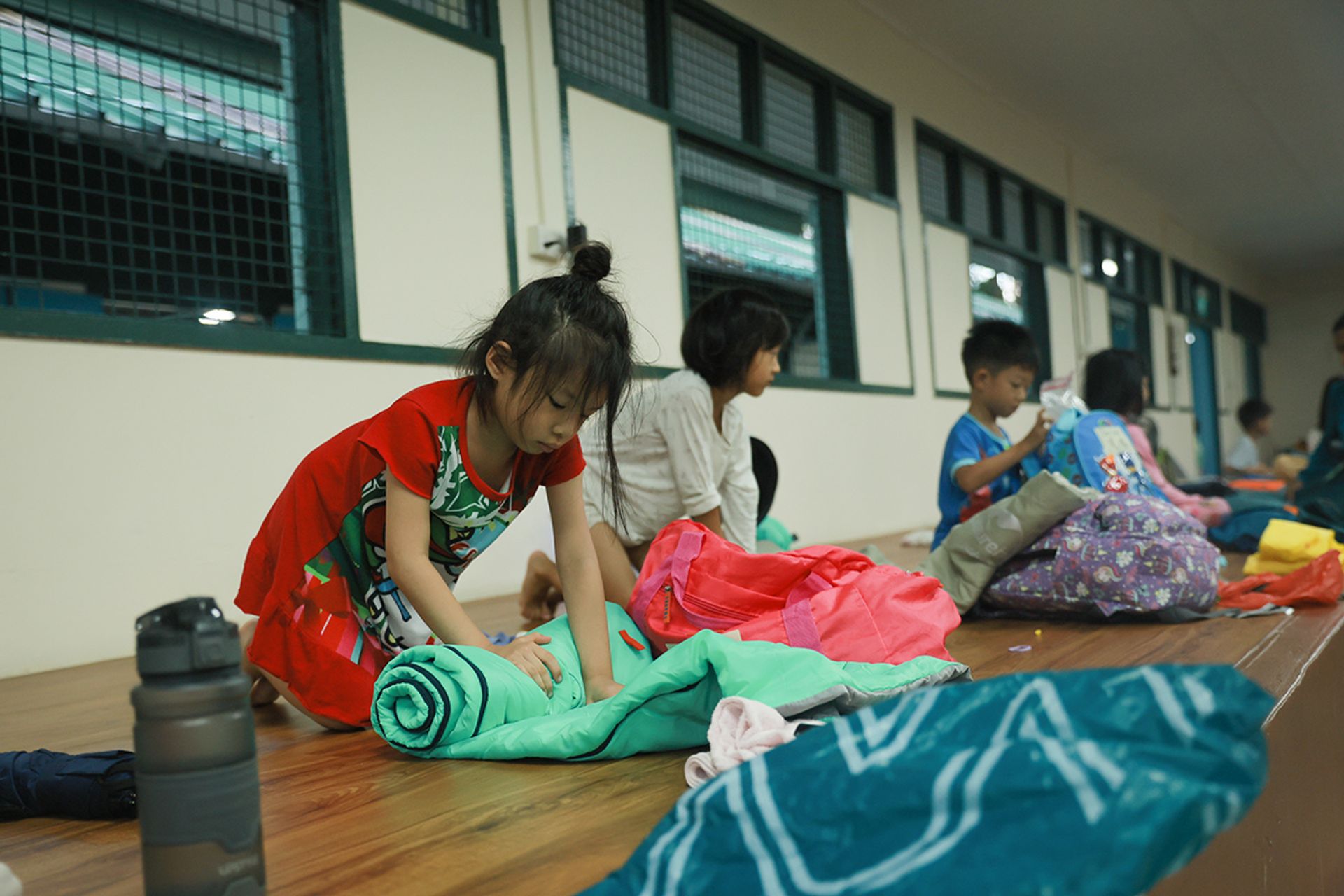 Ashley Oh (in red) rolls up her sleeping bag, as the children pack up to return home.