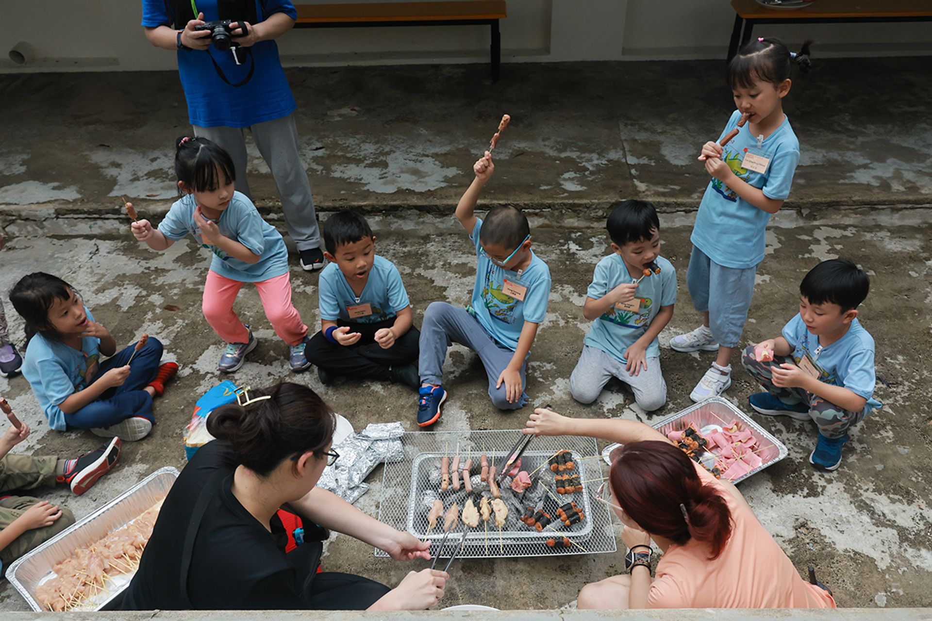 The adults help to grill the food skewers prepared by the children.