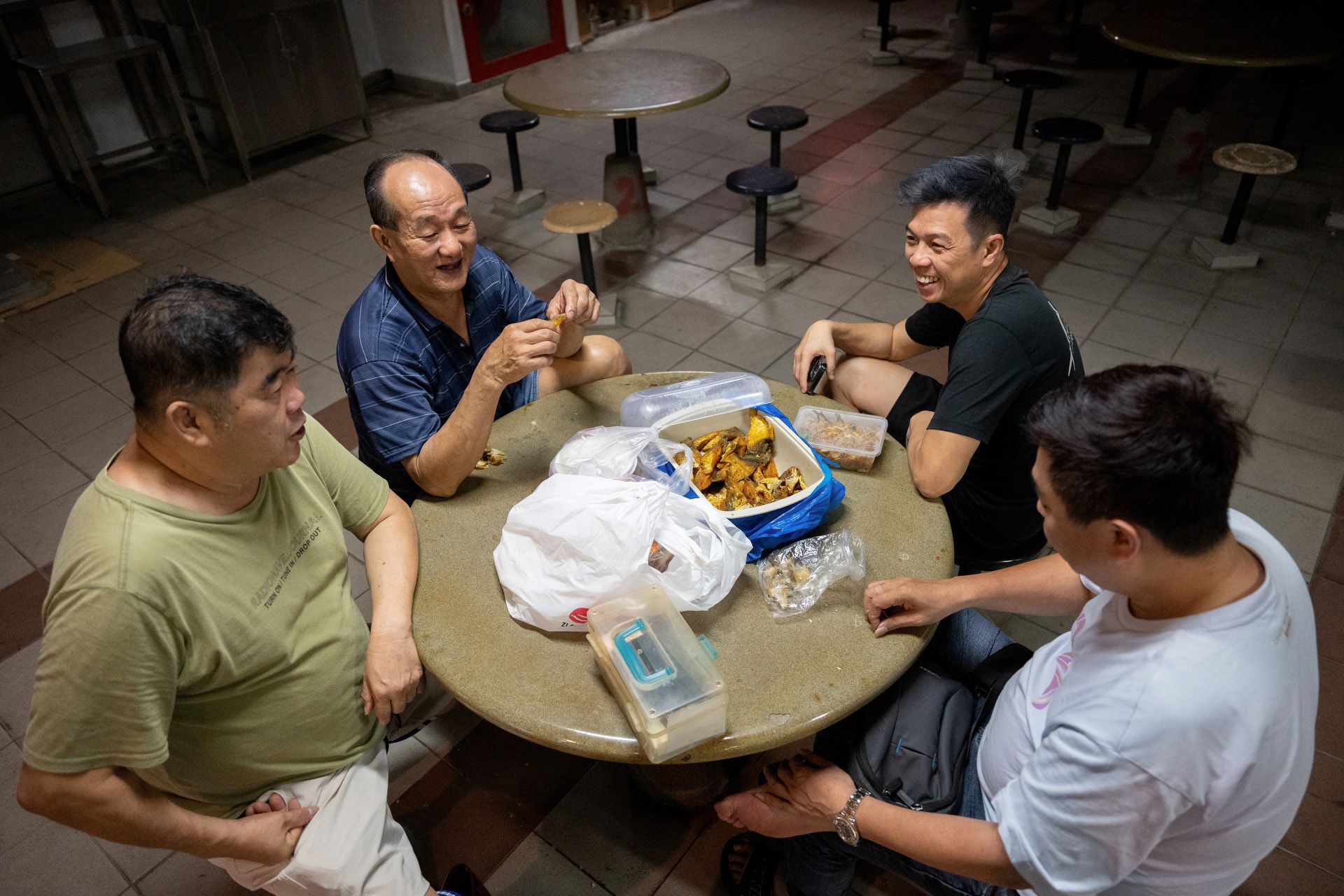 Fish merchants and workers chatting over fried fish prepared in Johor Bahru by a worker of fish merchant Gavin Chua (in white).