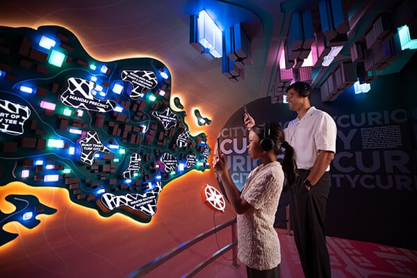 Two people in headphones interacting with a glowing city map exhibit.
