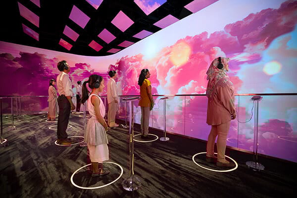 People in headphones gaze at a vibrant pink cloud display in an immersive exhibit.