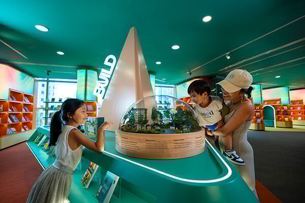 Family and two children admiring a miniature building and nature model.