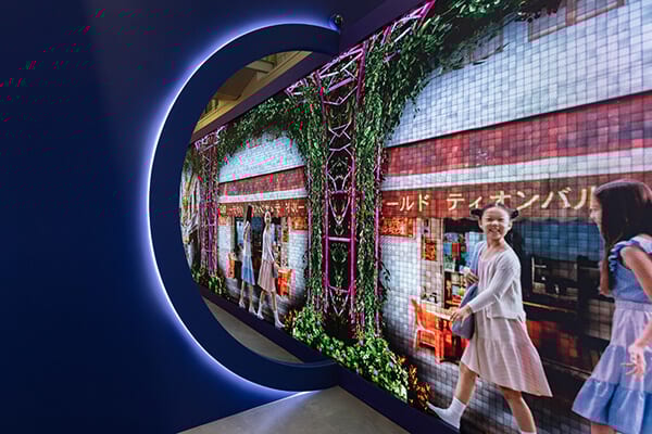 Digital display of a vibrant street scene with two girls, framed by a glowing circular opening.