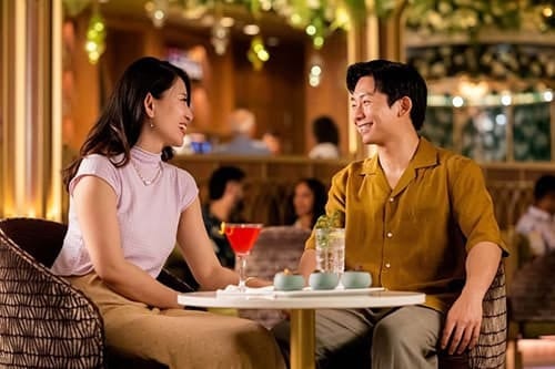 Smiling couple with drinks at a bar, looking at each other.