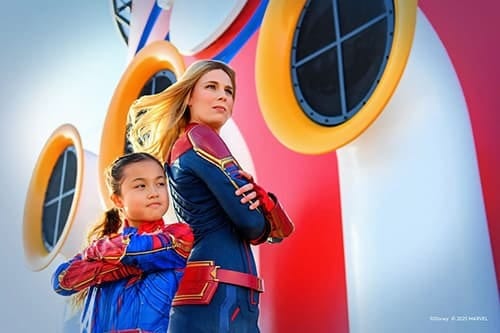 Adult and child dressed as Captain Marvel, standing heroically.