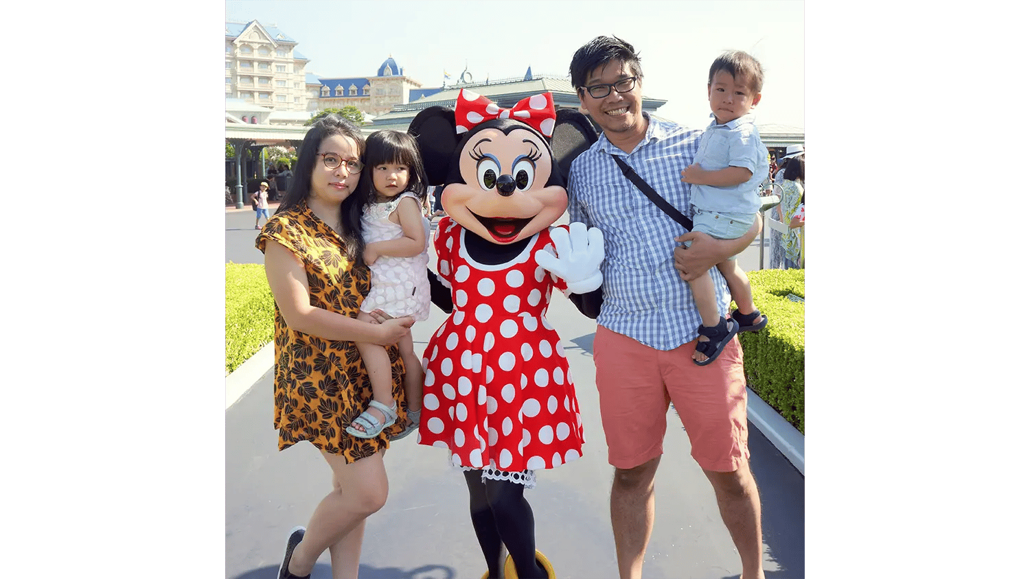 A family of four, including two young children, happily poses with Minnie Mouse at a theme park.