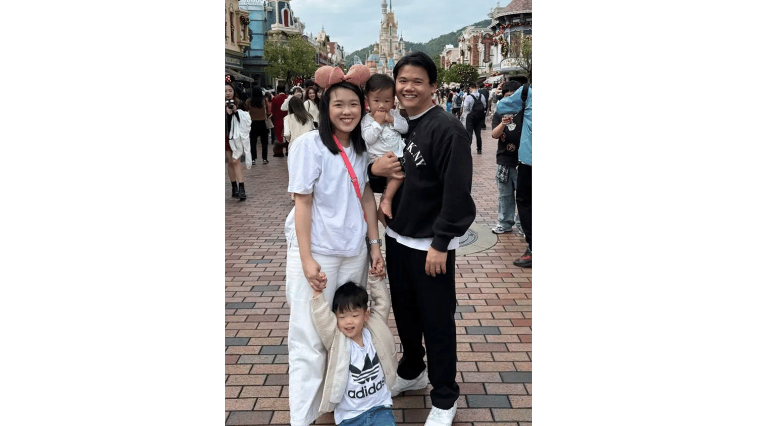 A family of four, including a man, woman, baby, and young boy, posing happily at Disneyland.