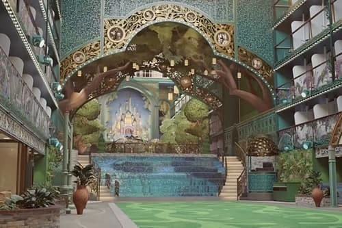 Lavish indoor space with a fantasy castle stage, turquoise pool, green floor, and ornate balconies.