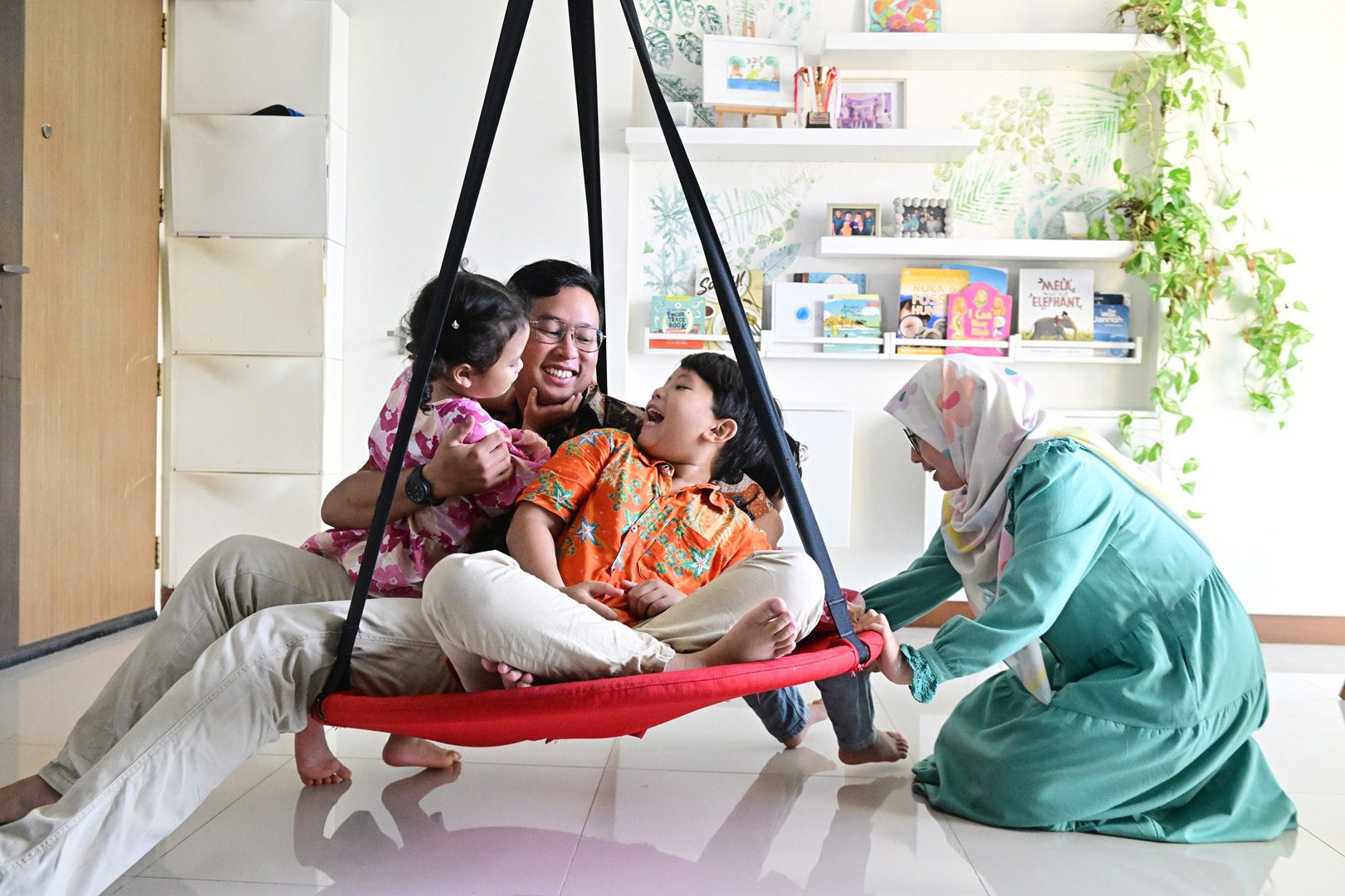 A joyful family with a father and two children on a swing, and a mother kneeling beside them.