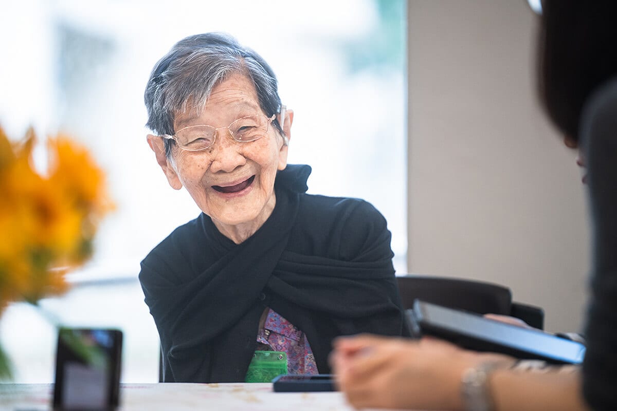 Happy elderly Asian woman with glasses and grey hair, laughing.
