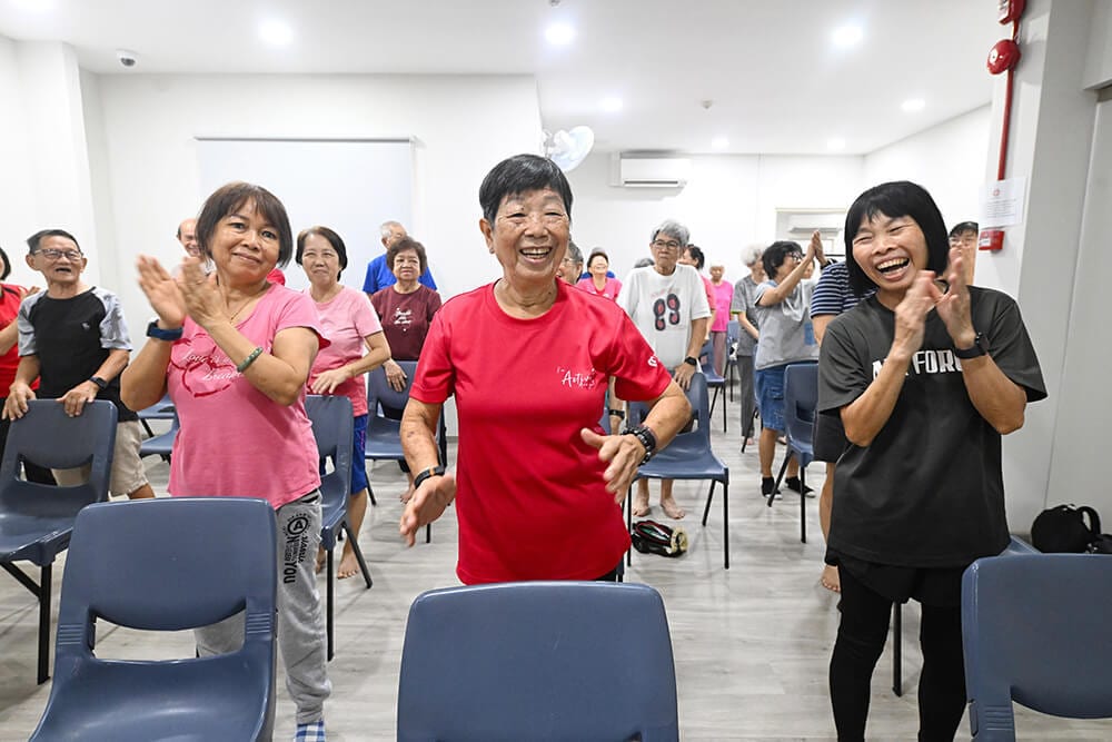 Elderly Asians joyfully exercising indoors, some clapping.