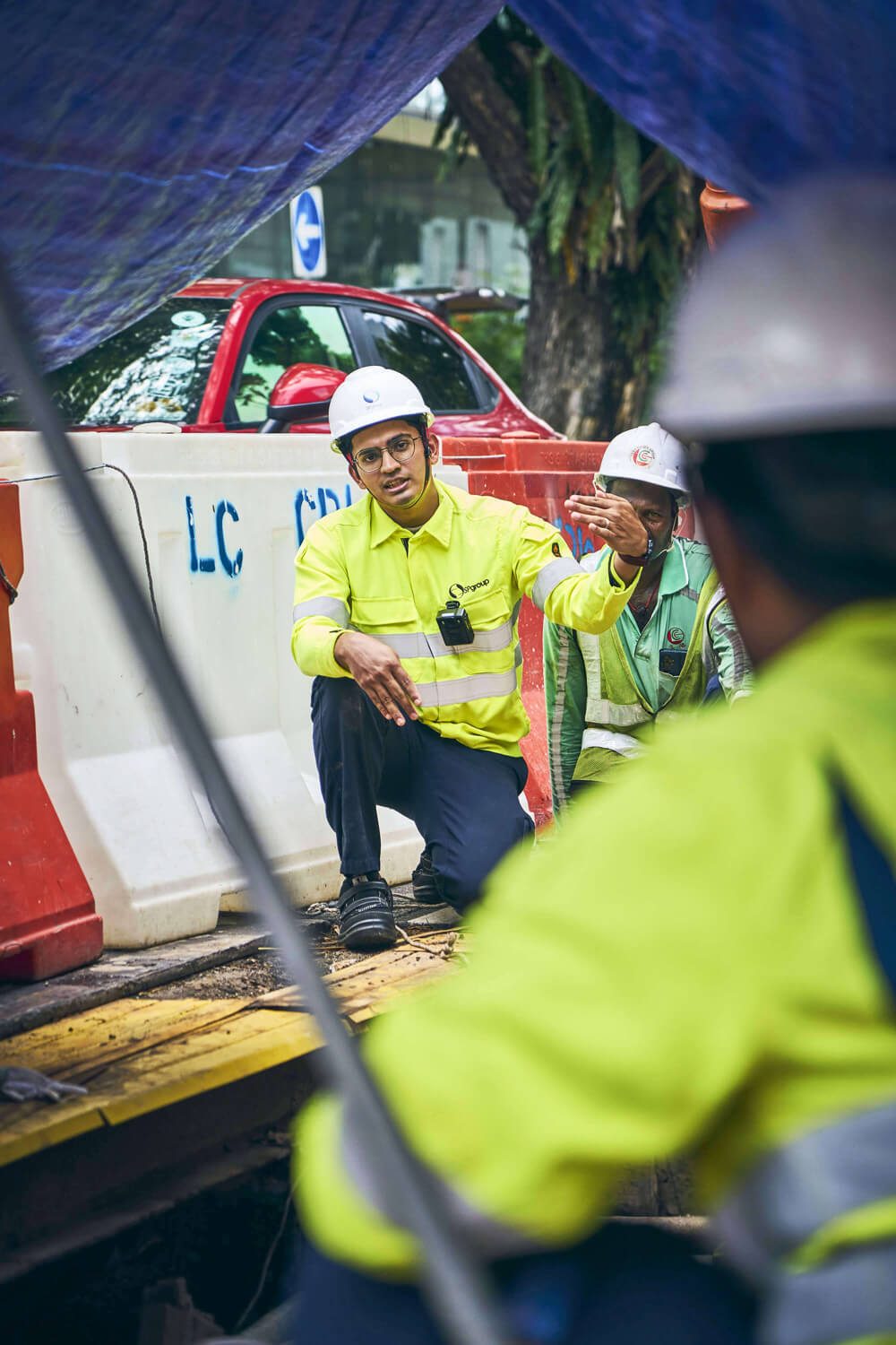 Construction workers in hard hats and safety vests discussing plans at a worksite.