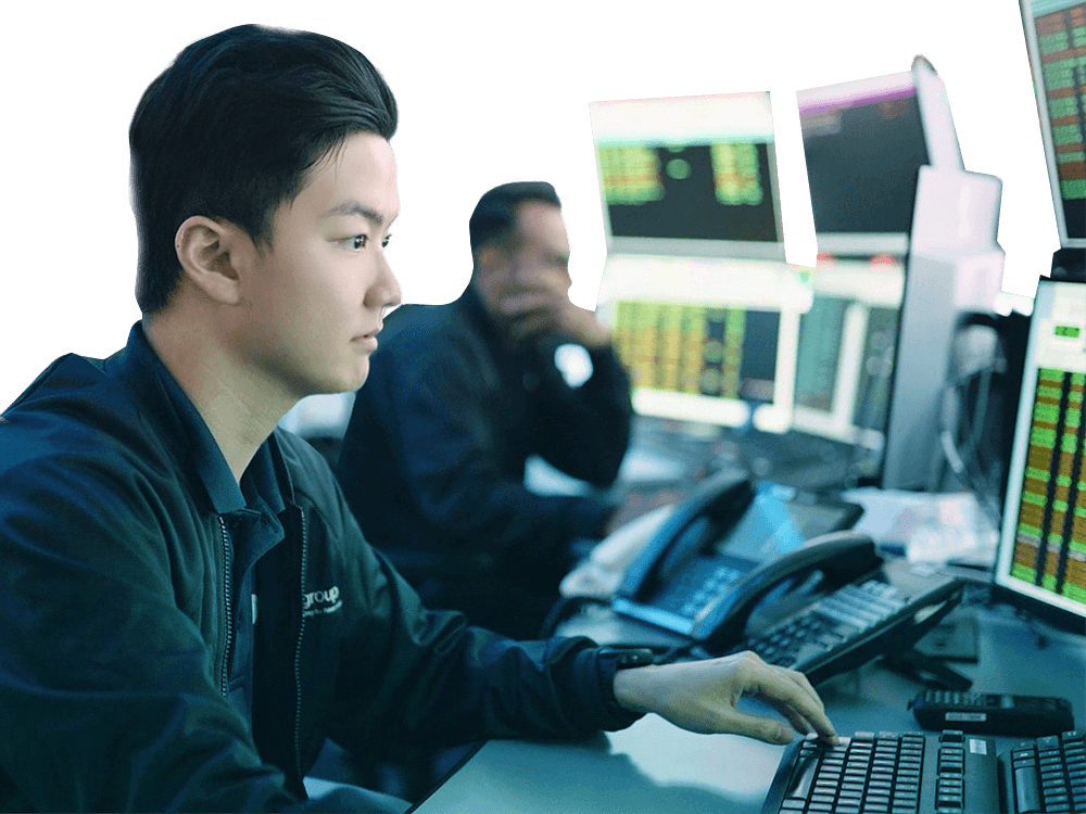 Young man in a control room, intently monitoring multiple computer screens and typing on a keyboard.