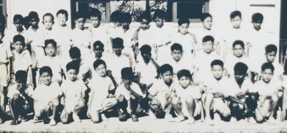 Vintage black and white photo of young Asian boys, some standing, some squatting.