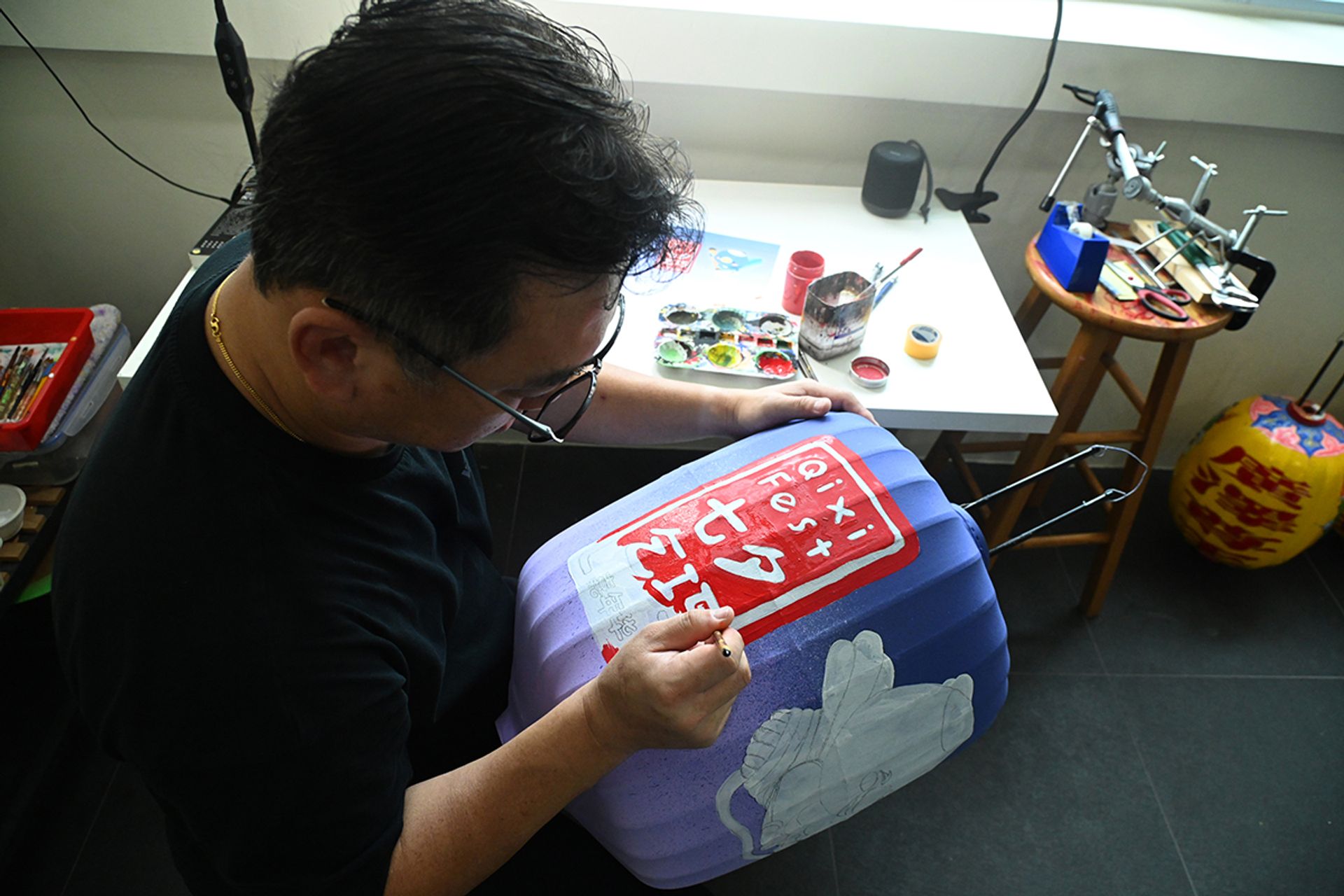 Mr Yeo painting the Chinese seal-style emblem of Qixi Fest in red acrylic paint.