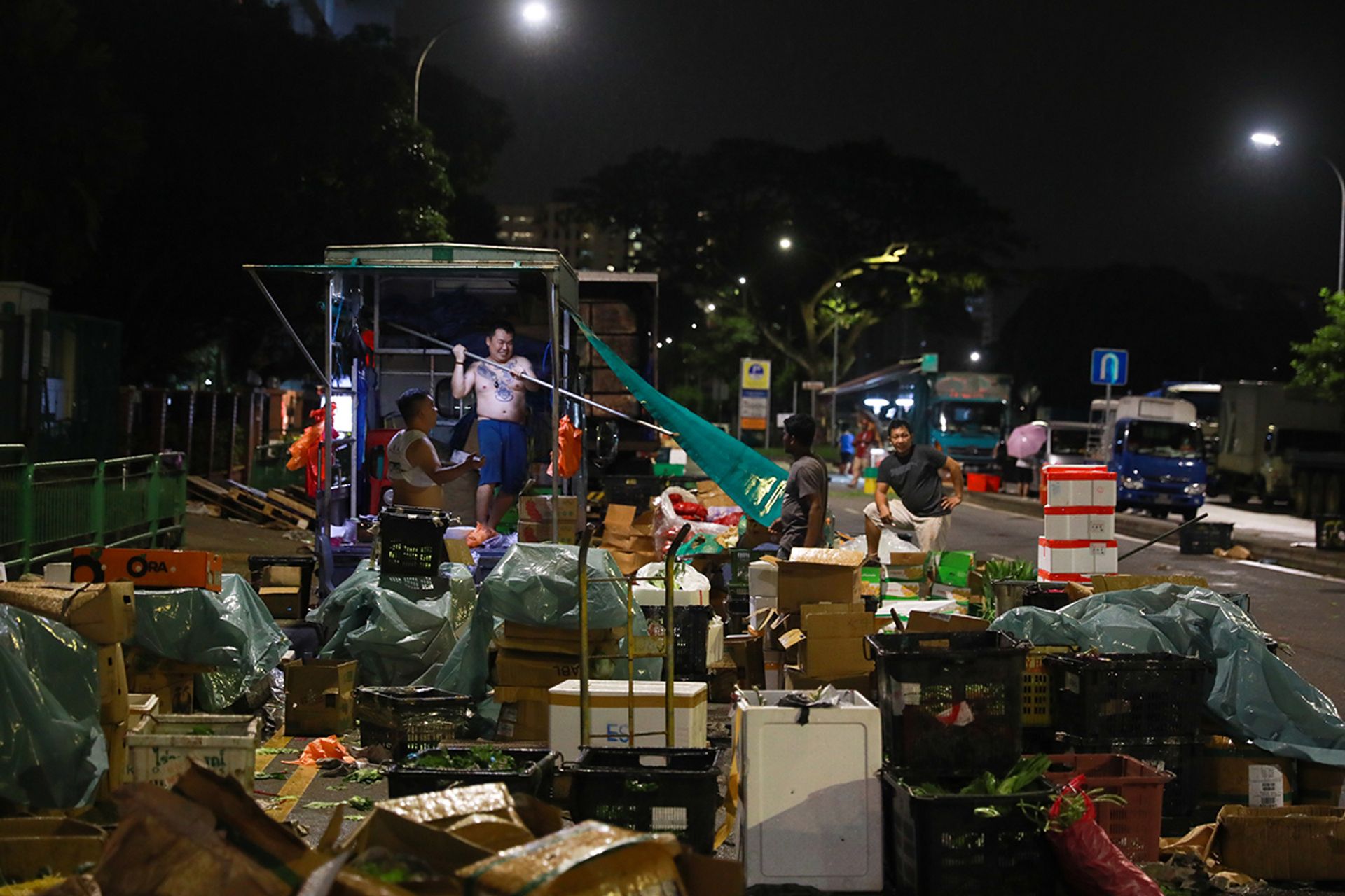 Mr Tan Teng Kuan (second from left), 33, setting up shelter on Mr Ong Chai Meng’s (far left) lorry as rain begins to fall. “I won’t miss this place, because there’s no shelter when it rains,” he said.