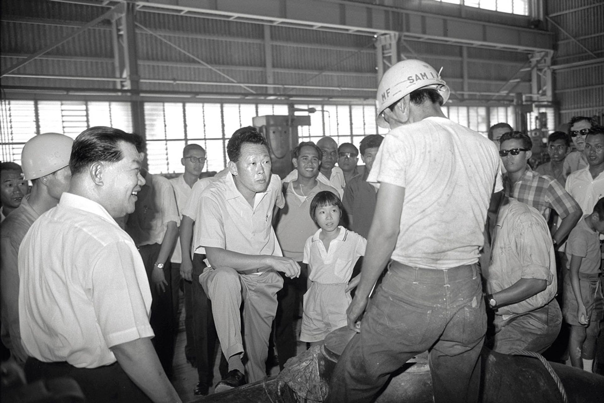 Mr Lee, accompanied by his daughter Wei Ling (centre), listening to a worker talk about his job at a factory in Jurong during a visit to the industrial estate in 1965. Source: MCI Collection