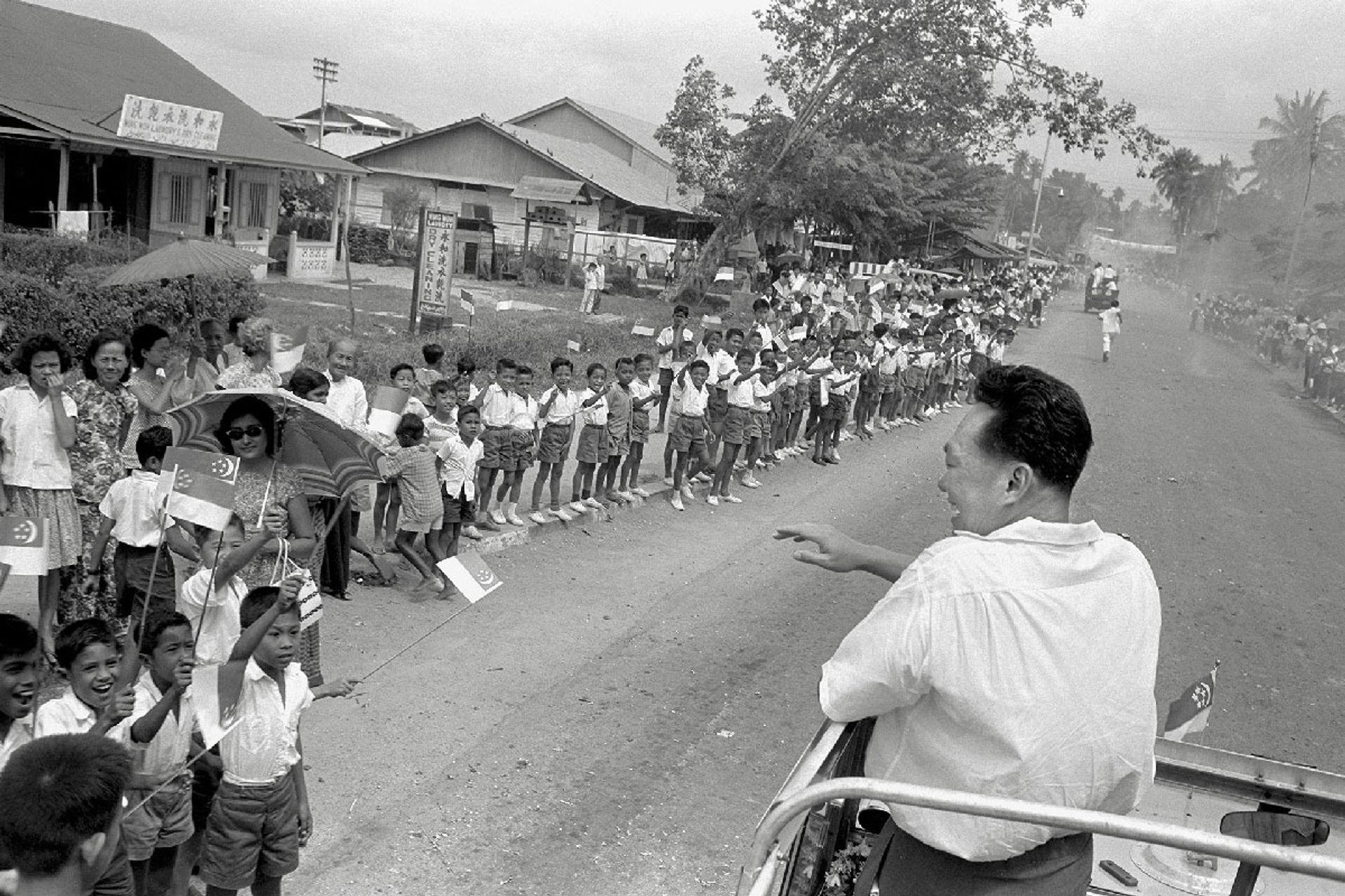 Mr Lee waving to schoolchildren from his campaign vehicle during his tour of Kampong Kembangan on Jan 12, 1963. Source: MCI collection