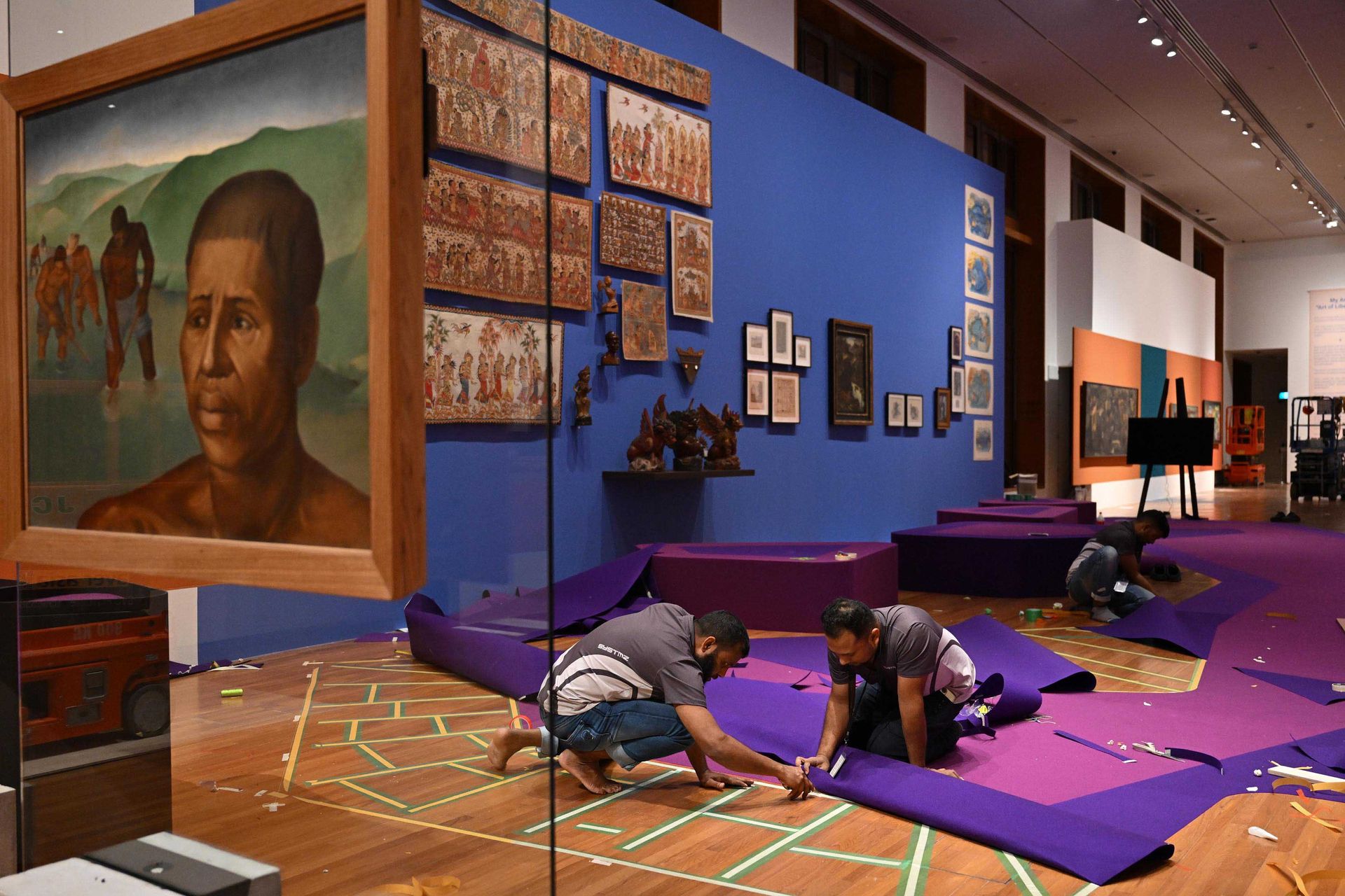 Workers fix parts of a carpet in front of the painting Trabalhadores (Portuguese for workers) by Brazilian painter Tarsila do Amaral.