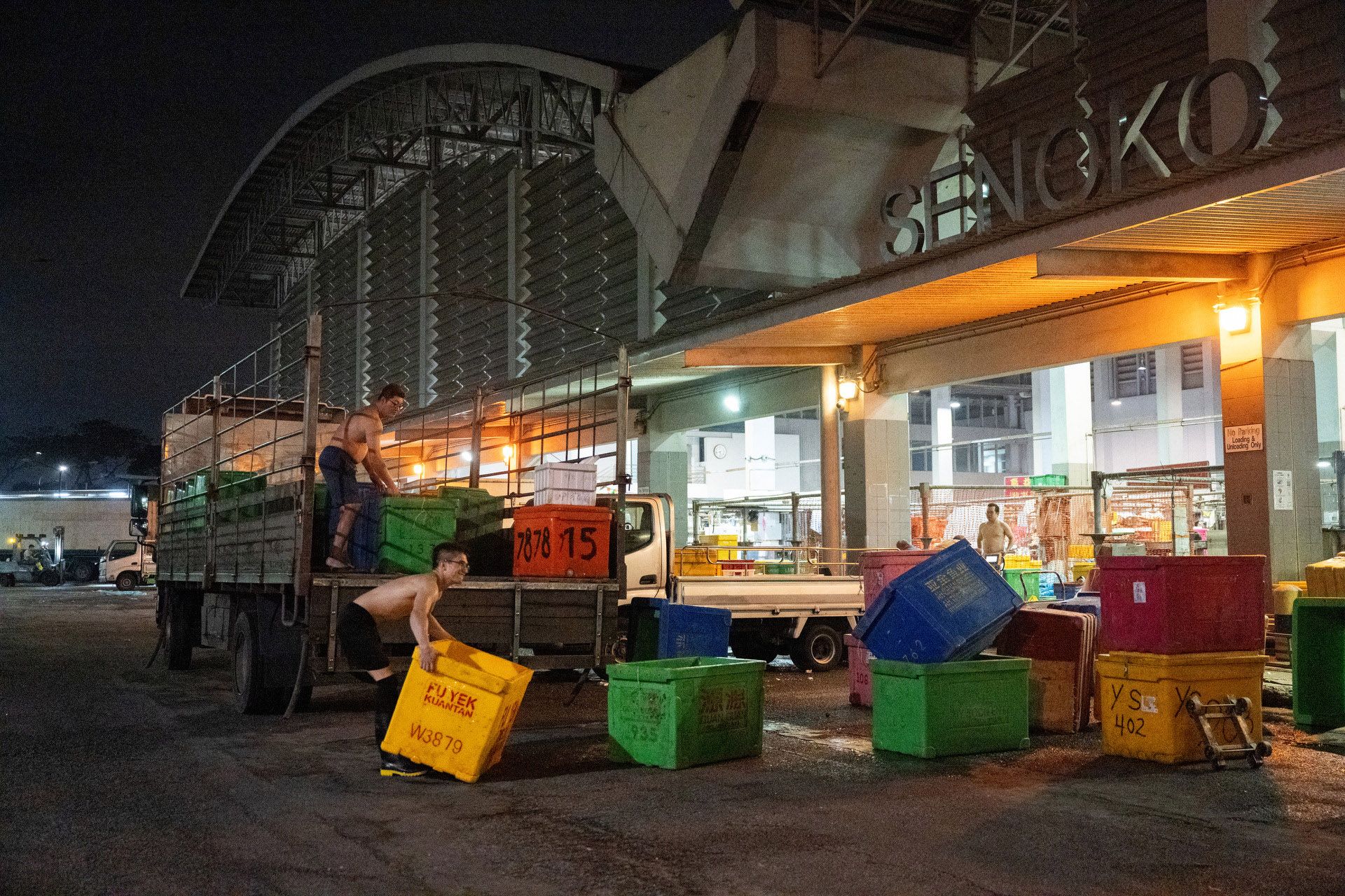 Two workers loading empty containers into a lorry in preparation for a new load of fish.
