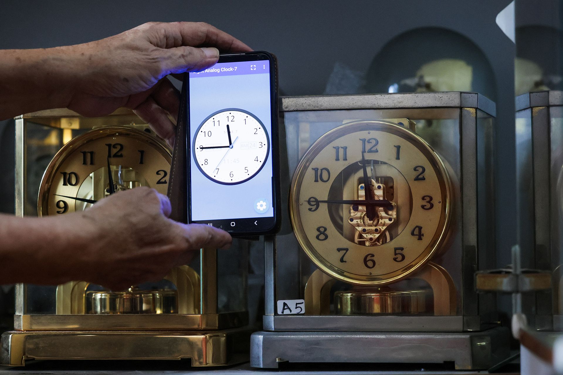 Mr Mun showing the accuracy of an ATMOS II (right) model, made in 1939, which very closely matches the time from a mobile phone. No mechanical clock can be accurate all the time, without some deviations.