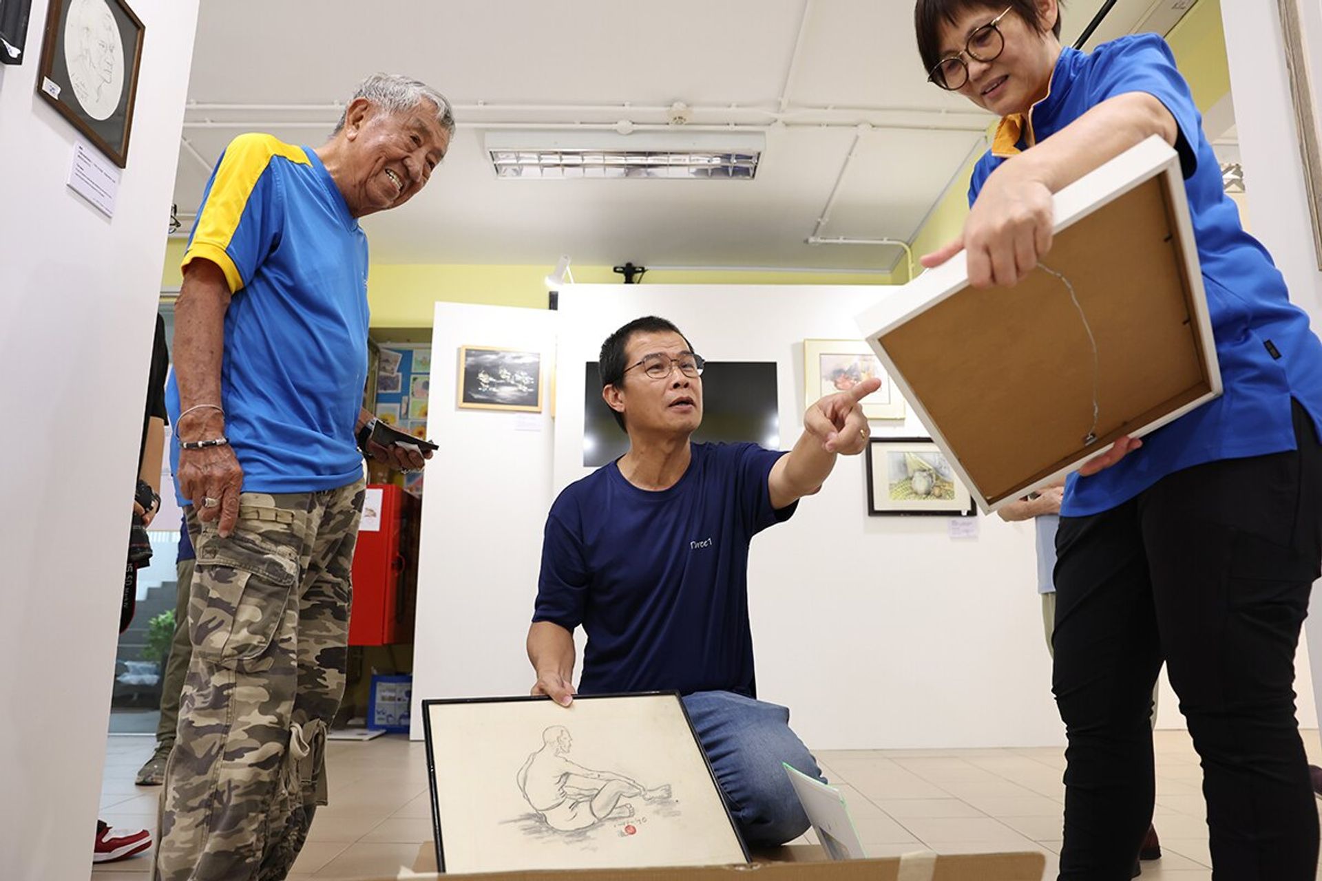 (From left) Mr Loke selecting artwork for the exhibition with the help of contractor Cheok Boon Teck, 53, and Ms Lee, 55, at the Precious Active Ageing Centre in Punggol, on May 30, 2024.