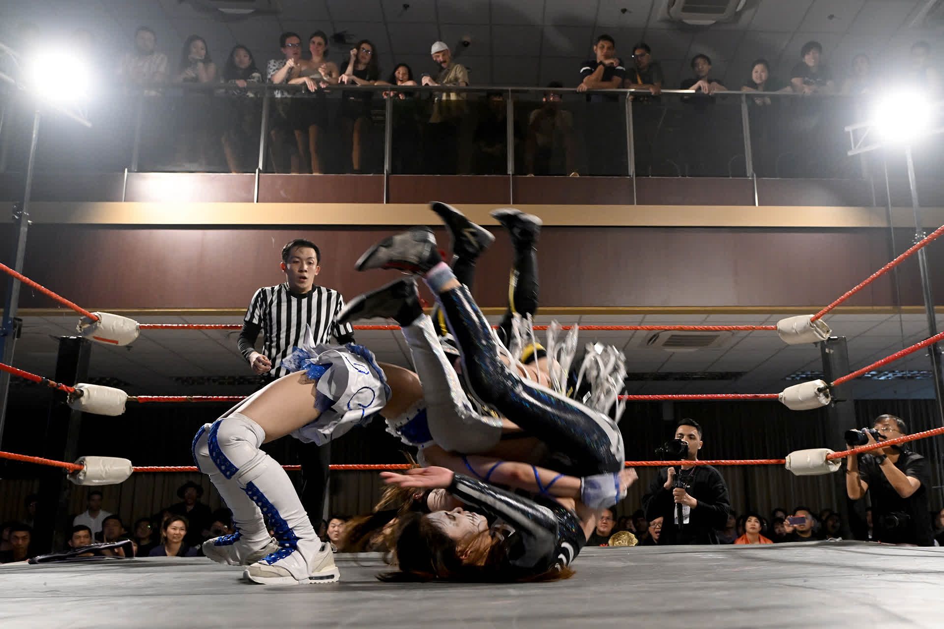 Riho (top) executing her trademark “Northern Light” suplex move on Lee. In the move, invented by Japanese professional wrestler turned politician Hiroshi Hase, the attacking wrestler puts her head under the arm of the opponent, wraps her arms around the waist, and flips the opponent backwards.