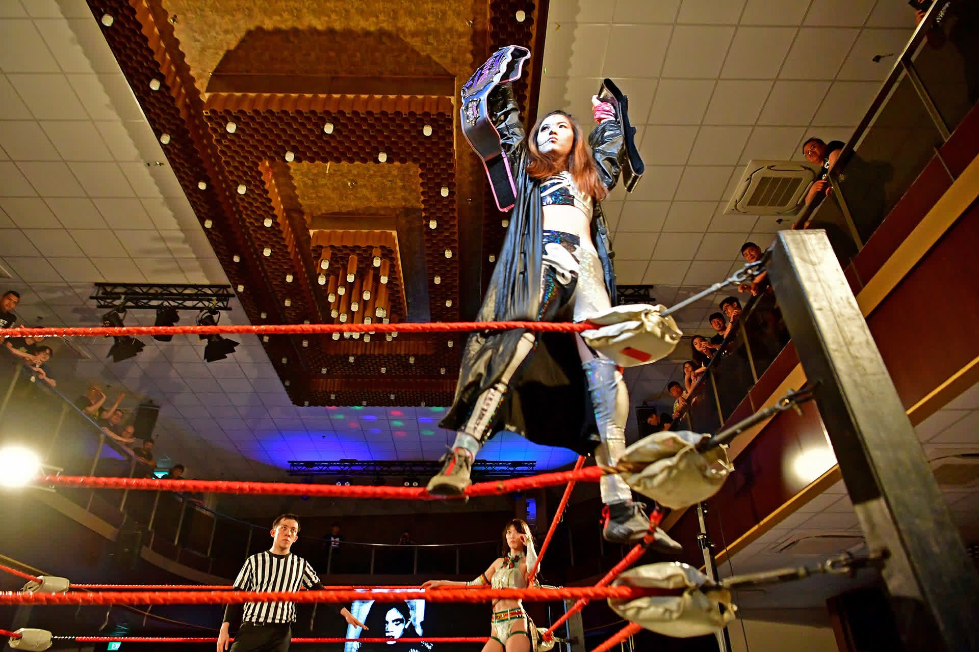 A victorious Lee climbing on the ropes and displaying her championship belts after winning her bout against Japanese wrestler Saki Akai at the Foochow Building on May 26, 2023.