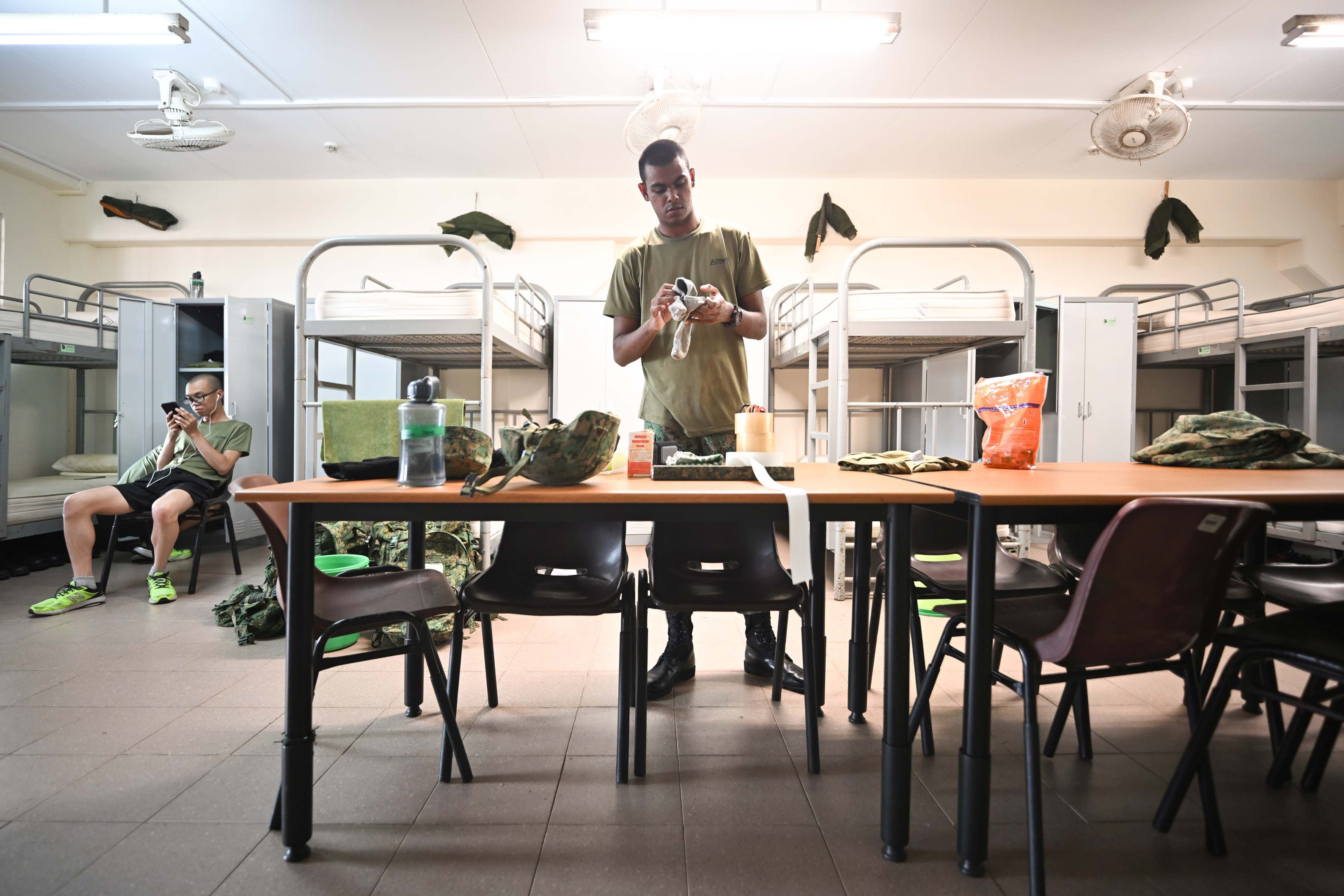 A man in the middle of a room with bunk beds at the Basic Military Training Centre on Pulau Tekong.