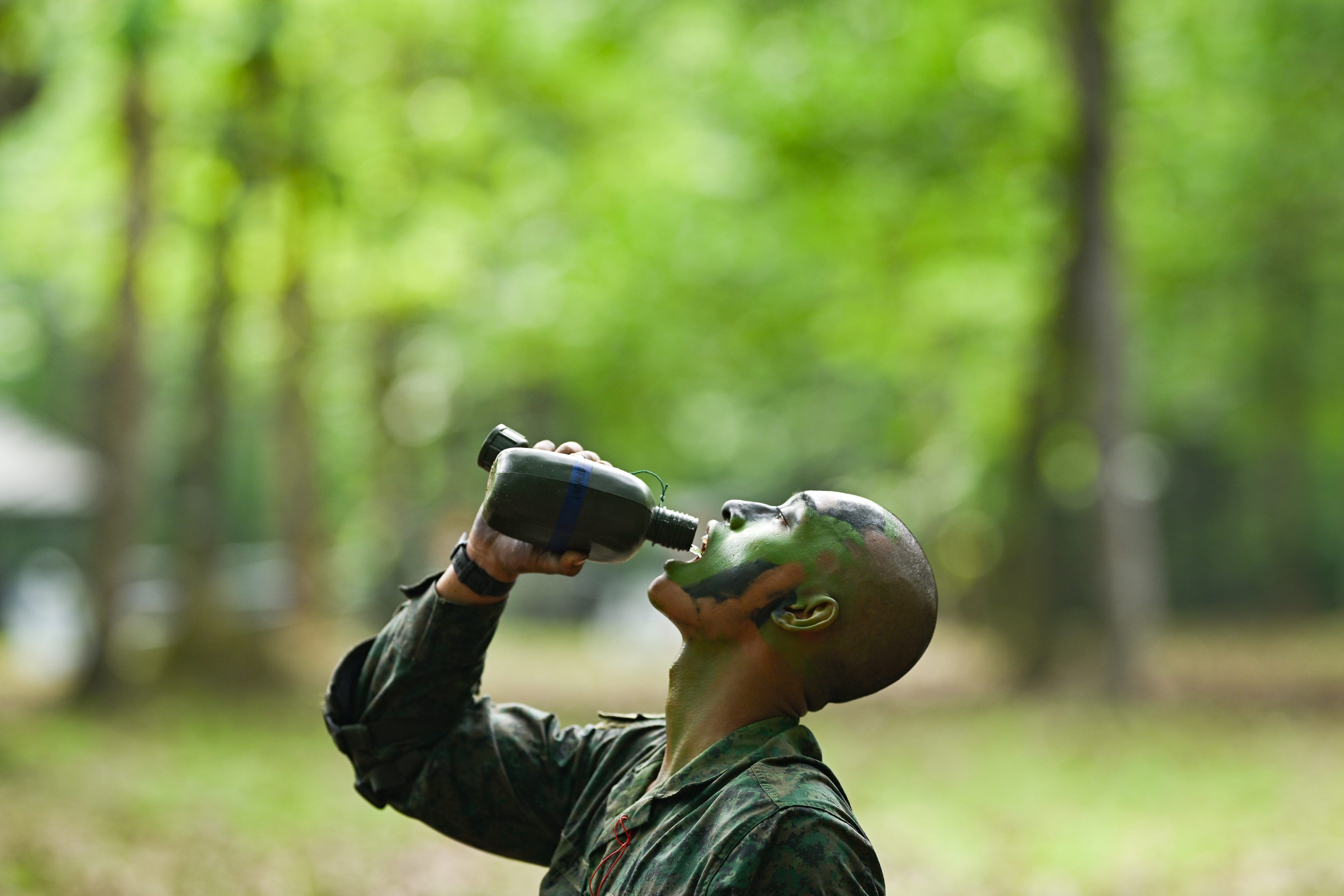 A man wearing a Singapore army uniform drinks from a water bottle on Pulau Tekong