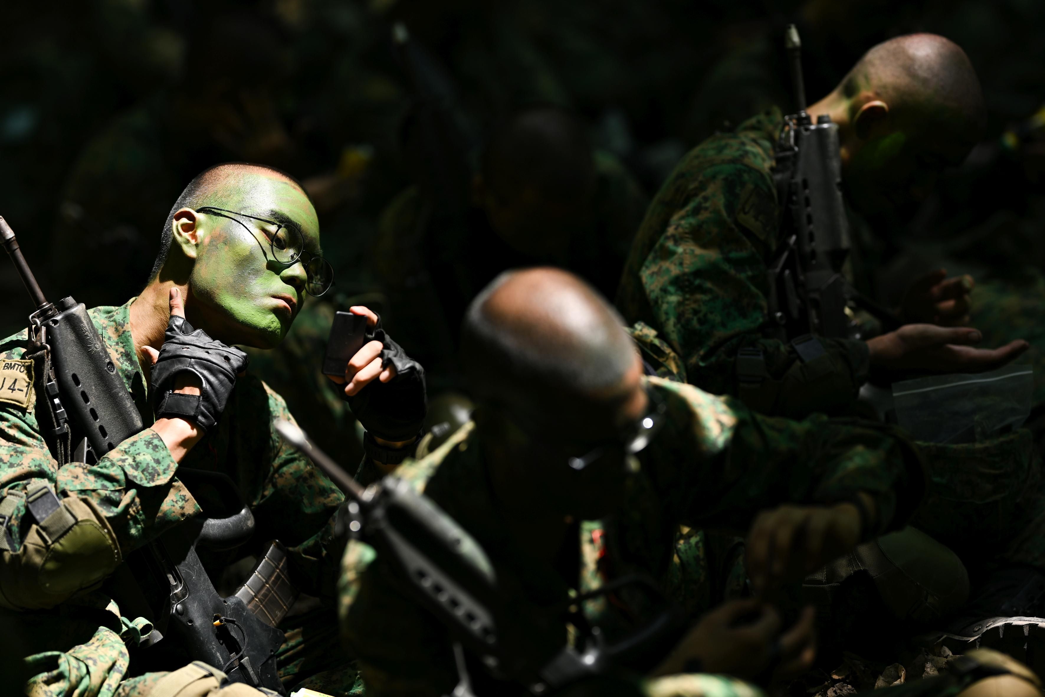 A group of men wearing the Singapore army uniform use camouflage cream on Pulau Tekong