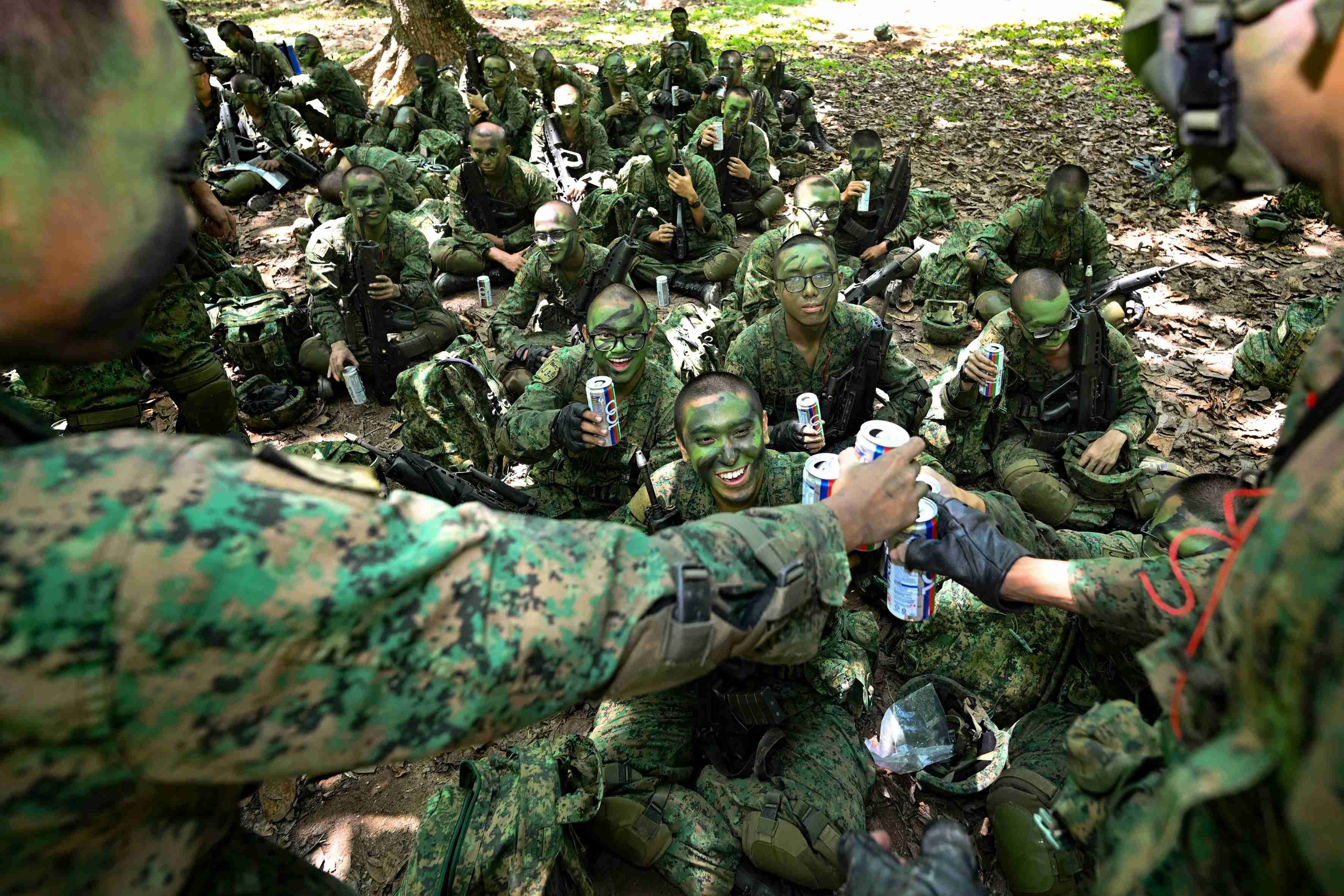 A group of men wearing the Singapore army uniform drink can drinks on Pulau Tekong