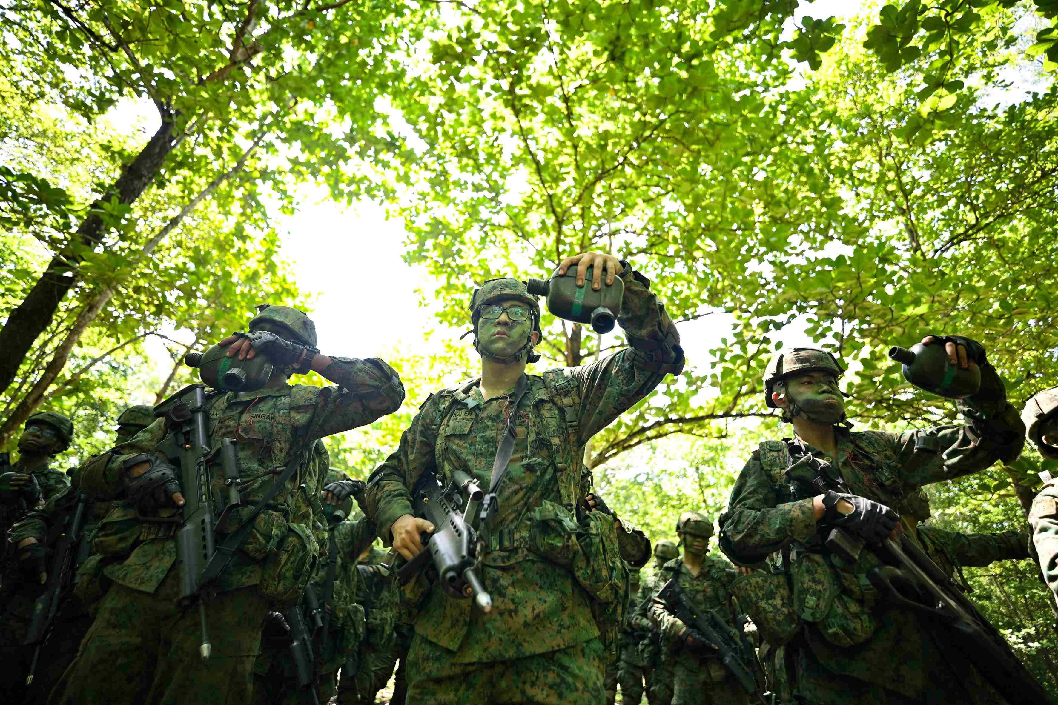 A group of men wearing a Singapore army uniforms upturn their water bottles after drinking water on Pulau Tekong