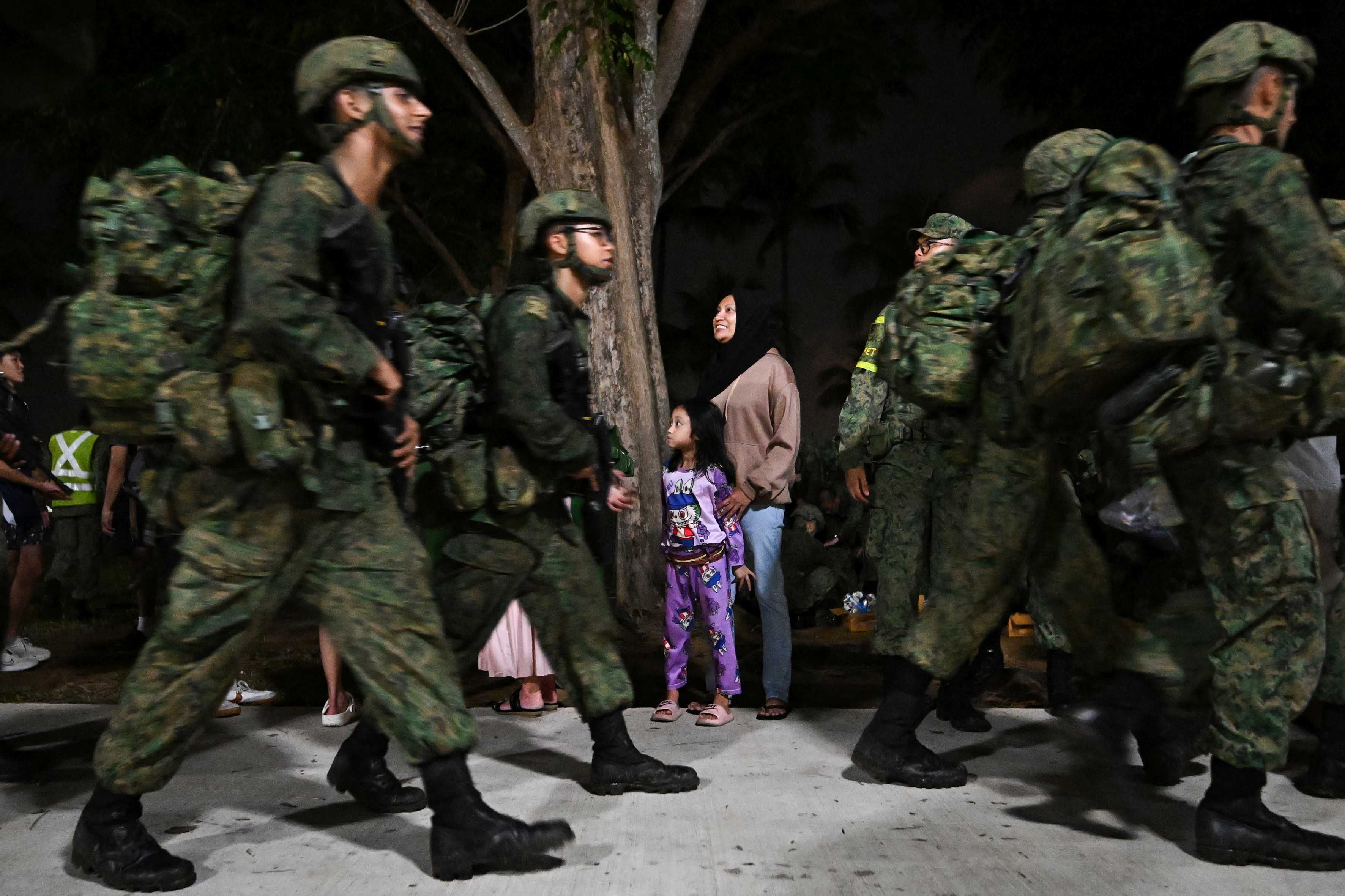 A woman and child look on as men in the Singapore army uniform walk past at East Coast Park