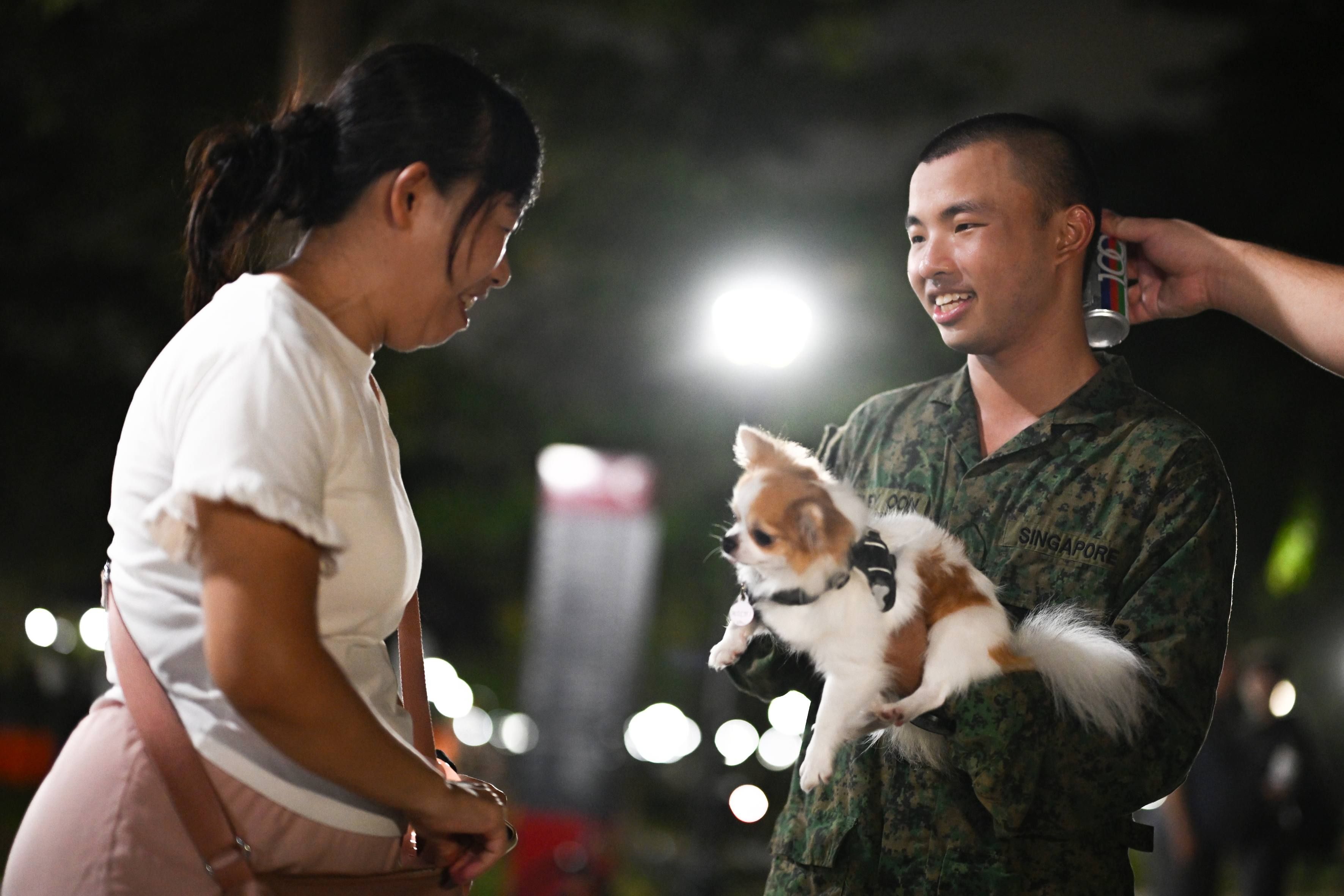 A man in a Singapore Army uniform and lady talk as he carries a pet dog at East Coast Park