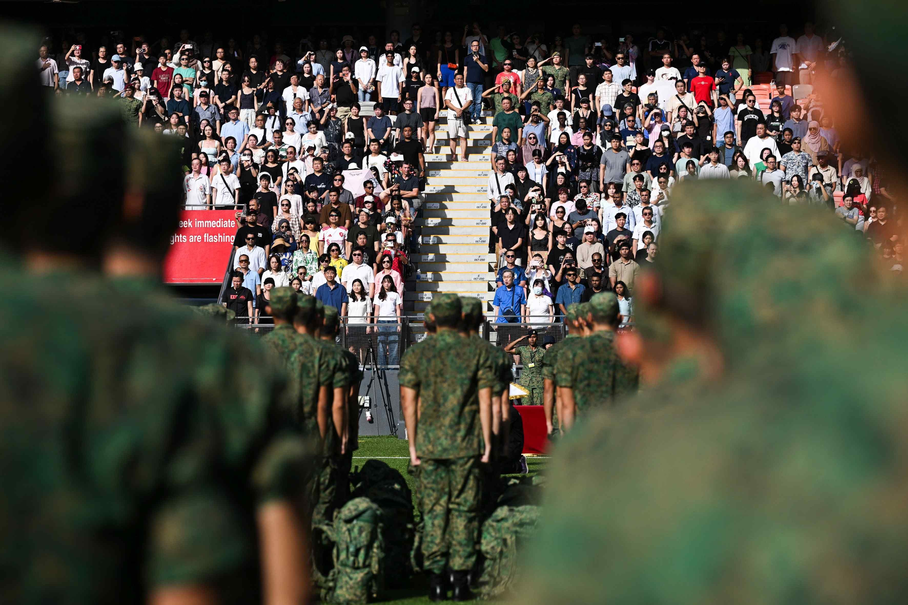 A crowd of people watch a parade march past at Our Tampines Hub