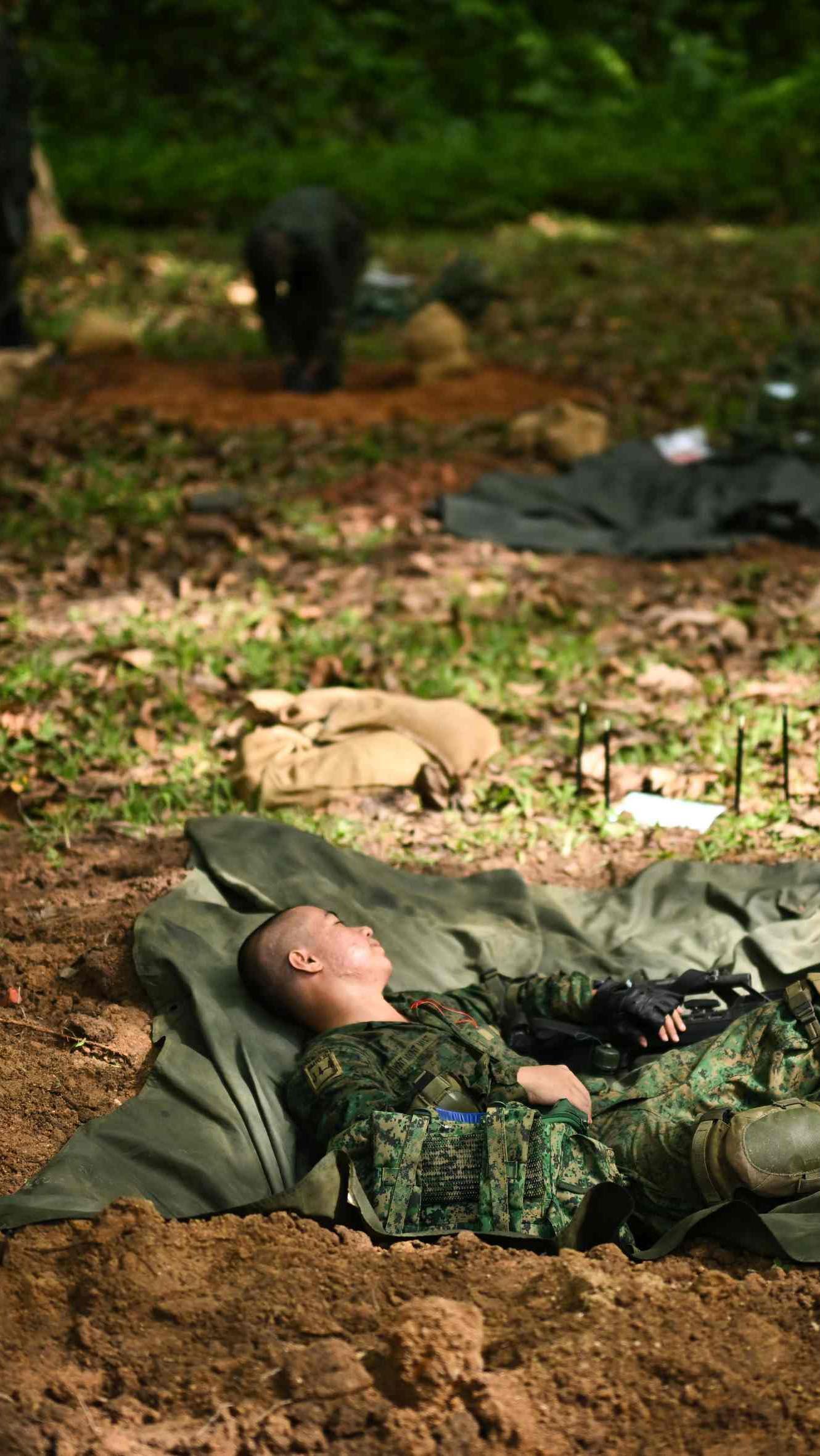 A man in a singapore army uniform rests in a shell scrape