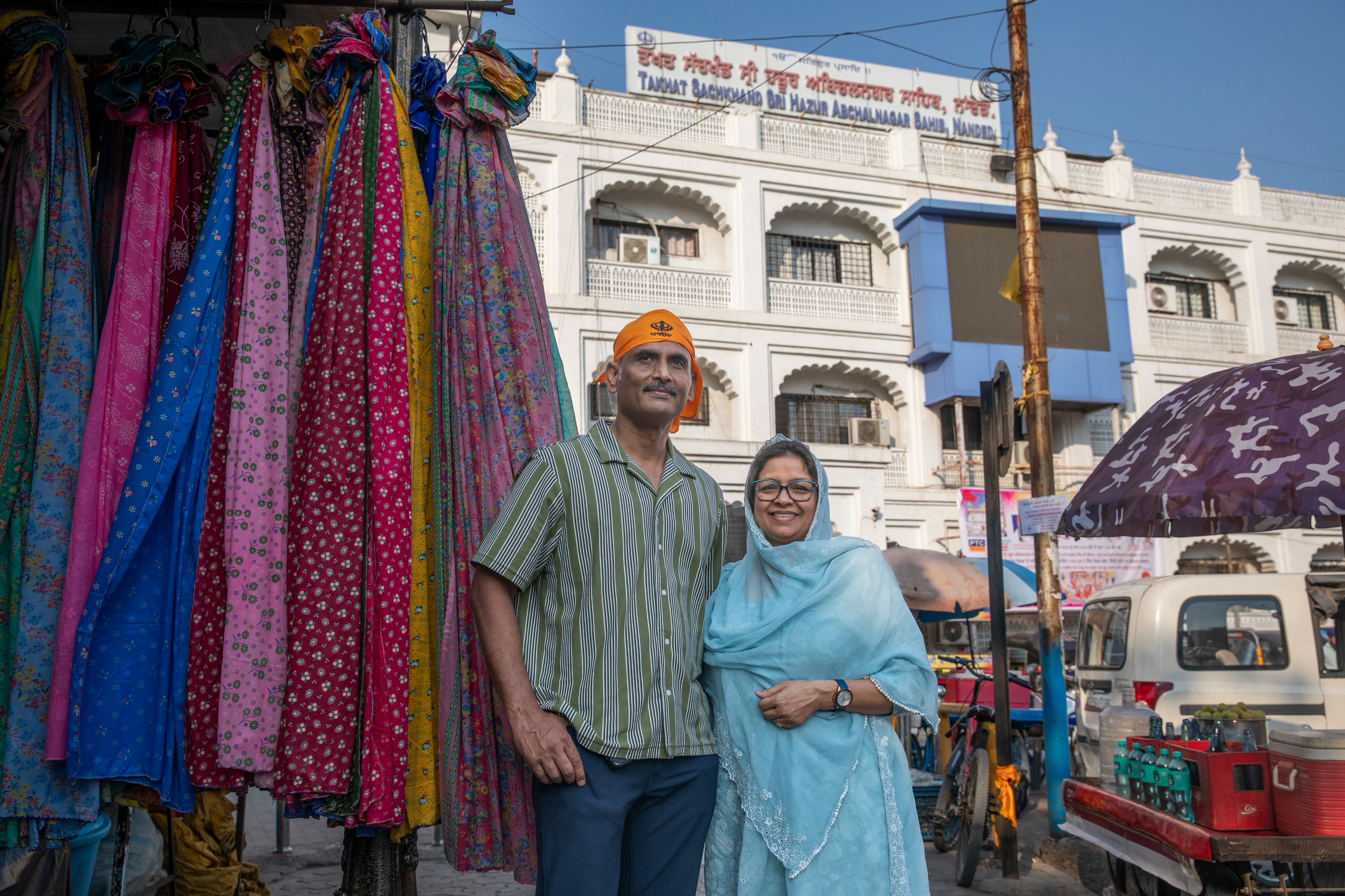 Jasmine Kaur, 54, in a light blue outfit, and her husband Ramesh, 57, to her left, pose with their heads covered in respect in front of the Takht Sachkhand Sri Hazur Abchalnagar Sahib, a Sikh religious site in Nanded, Maharashtra state in India.