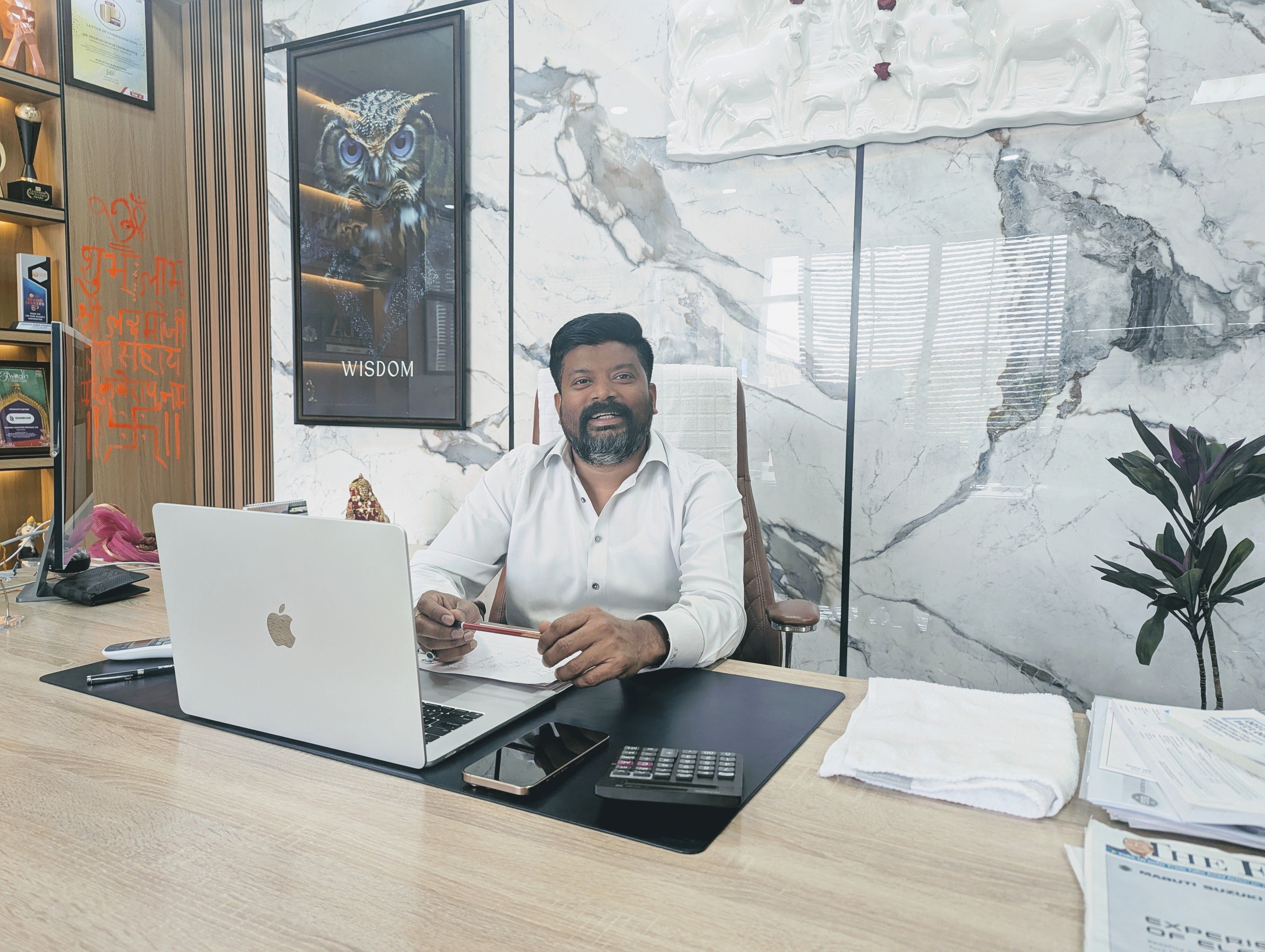 Shankh Air’s founder Shravan Kumar Vishwakarma is smiling at the camera, sitting at his desk in the Lucknow office with his laptop open. The room walls are made of white marble.