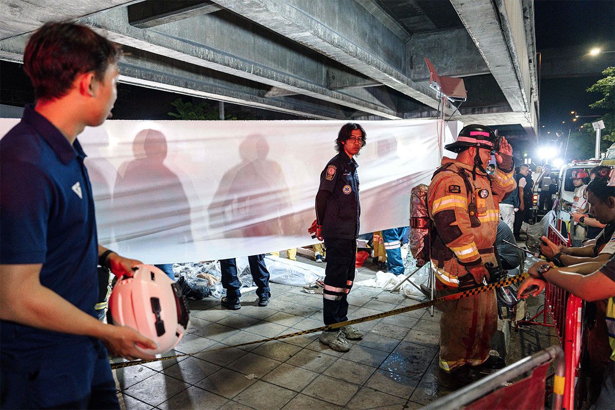 Emergency workers stand next to a white fabric displayed at the scene after a massive fire engulfed a bar in Bangkok, early on July 13, 2026.