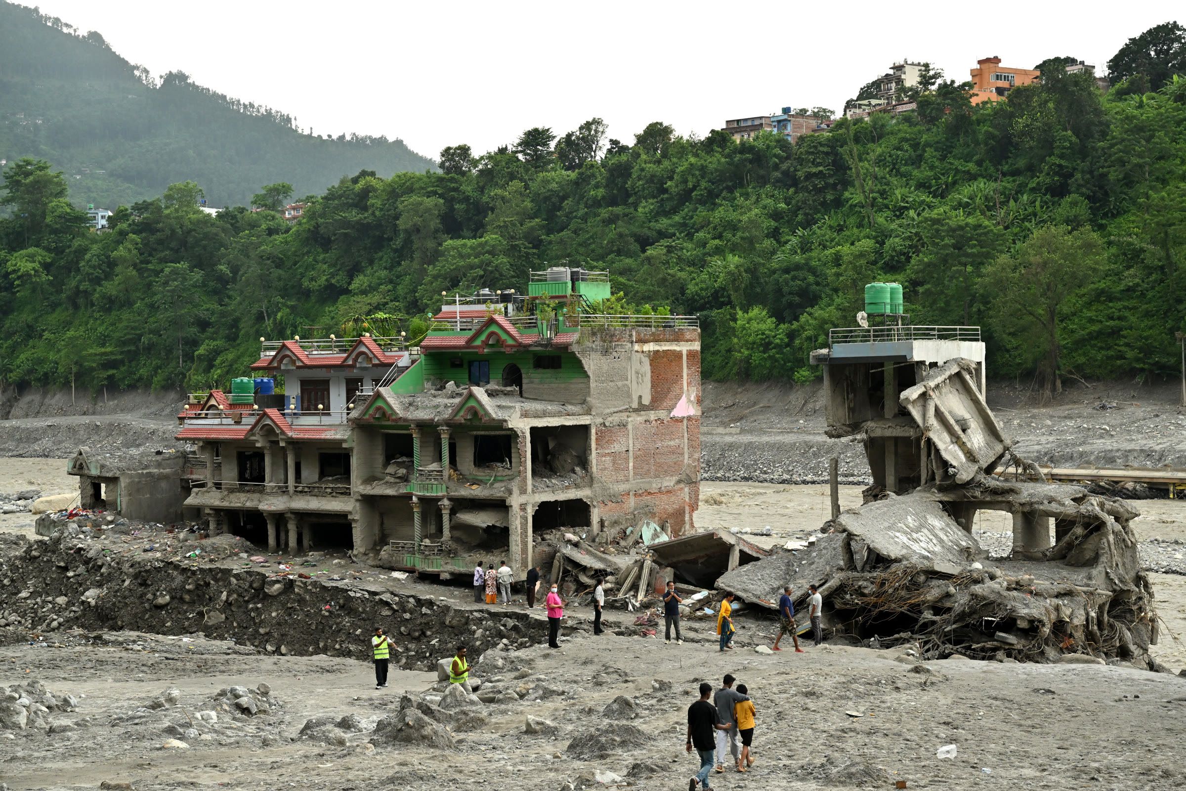 Residents walking among ruined concrete homes and debris in Trishuli Bazar, beside the Trishuli River.