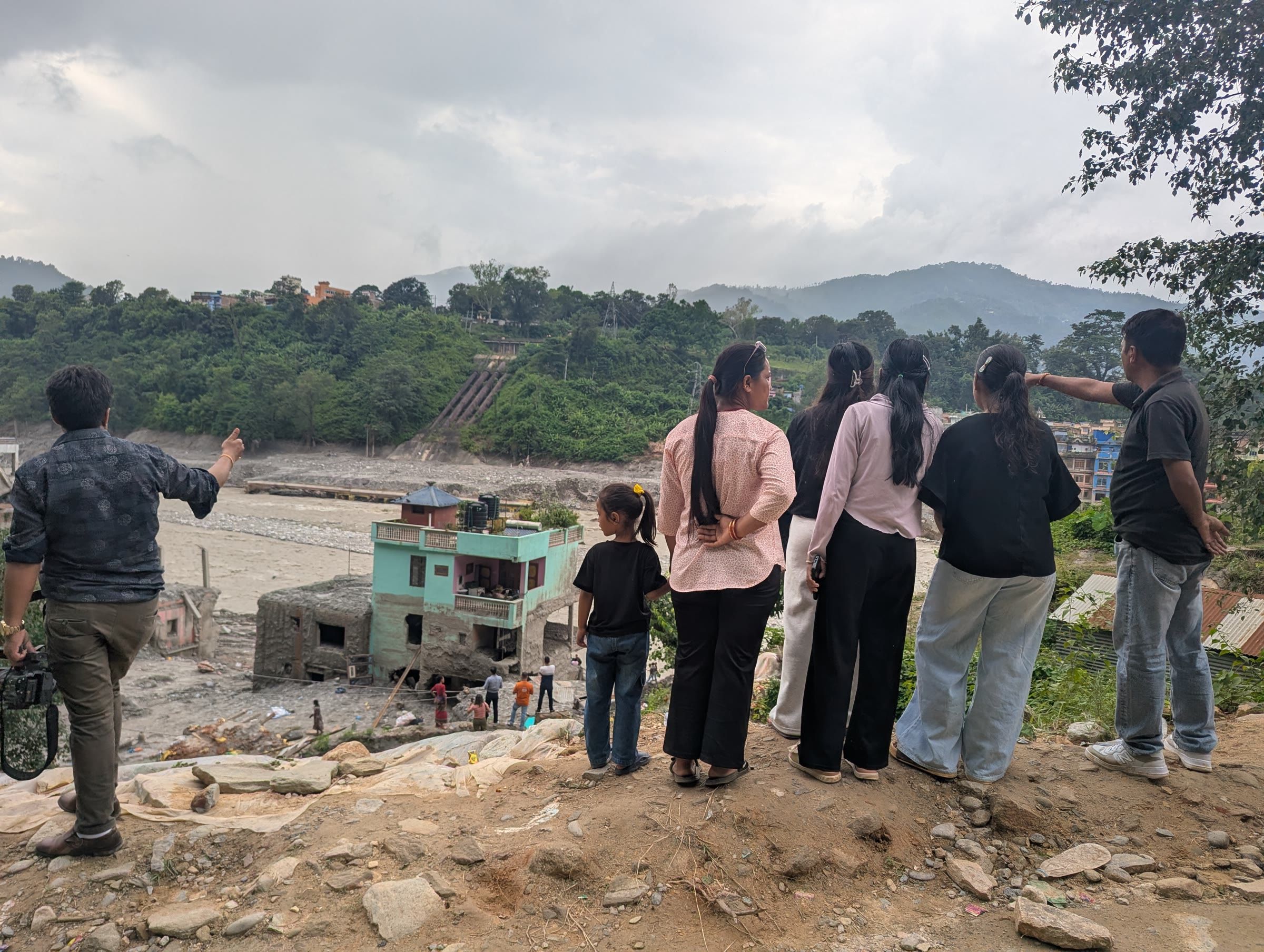 Visitors looking at flood-damaged areas and structures, including a mint-green house that remained standing, in Trishuli Bazar.