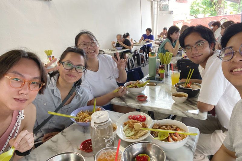 A selfie with 5 members of the team smiling with prawn noodles on the table.