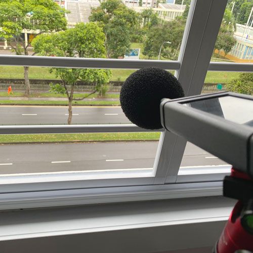 The sound meter on the tripod pointing down at the road from an open window